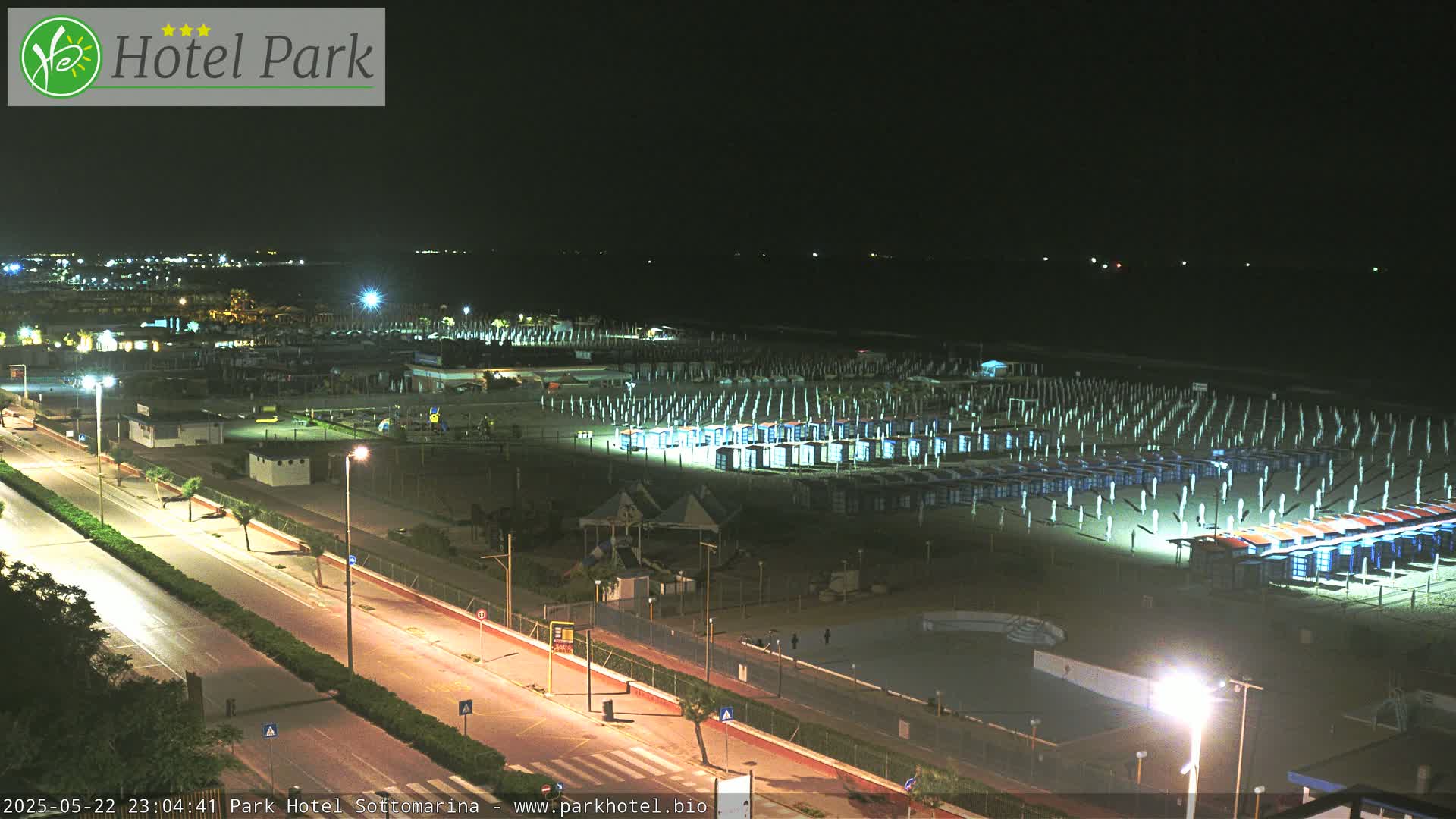 A nighttime view of a beach with rows of closed beach umbrellas and a road running parallel to the shore.