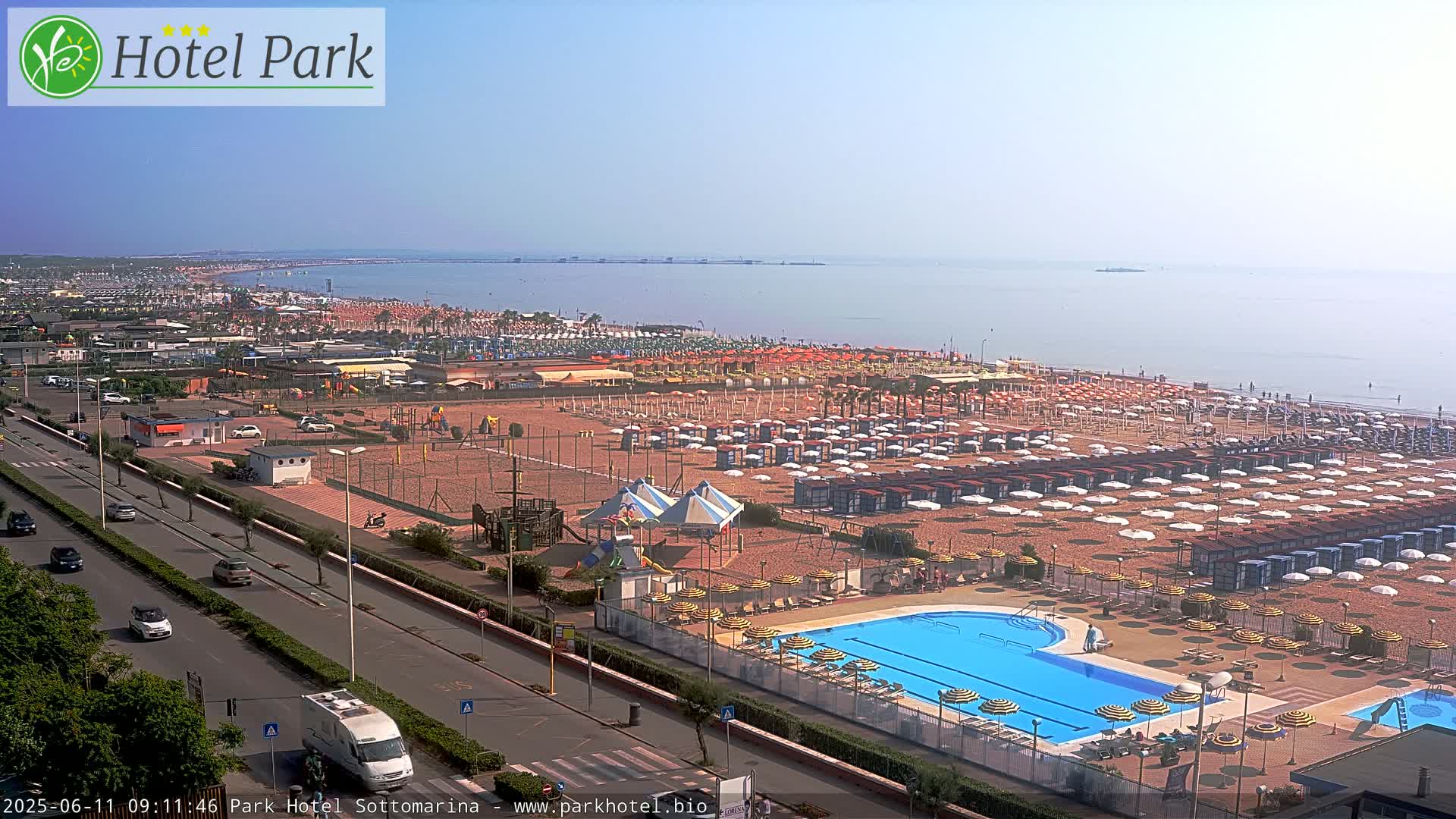 A beach resort with a swimming pool and numerous beach umbrellas is visible, overlooking a calm ocean on a hazy day.