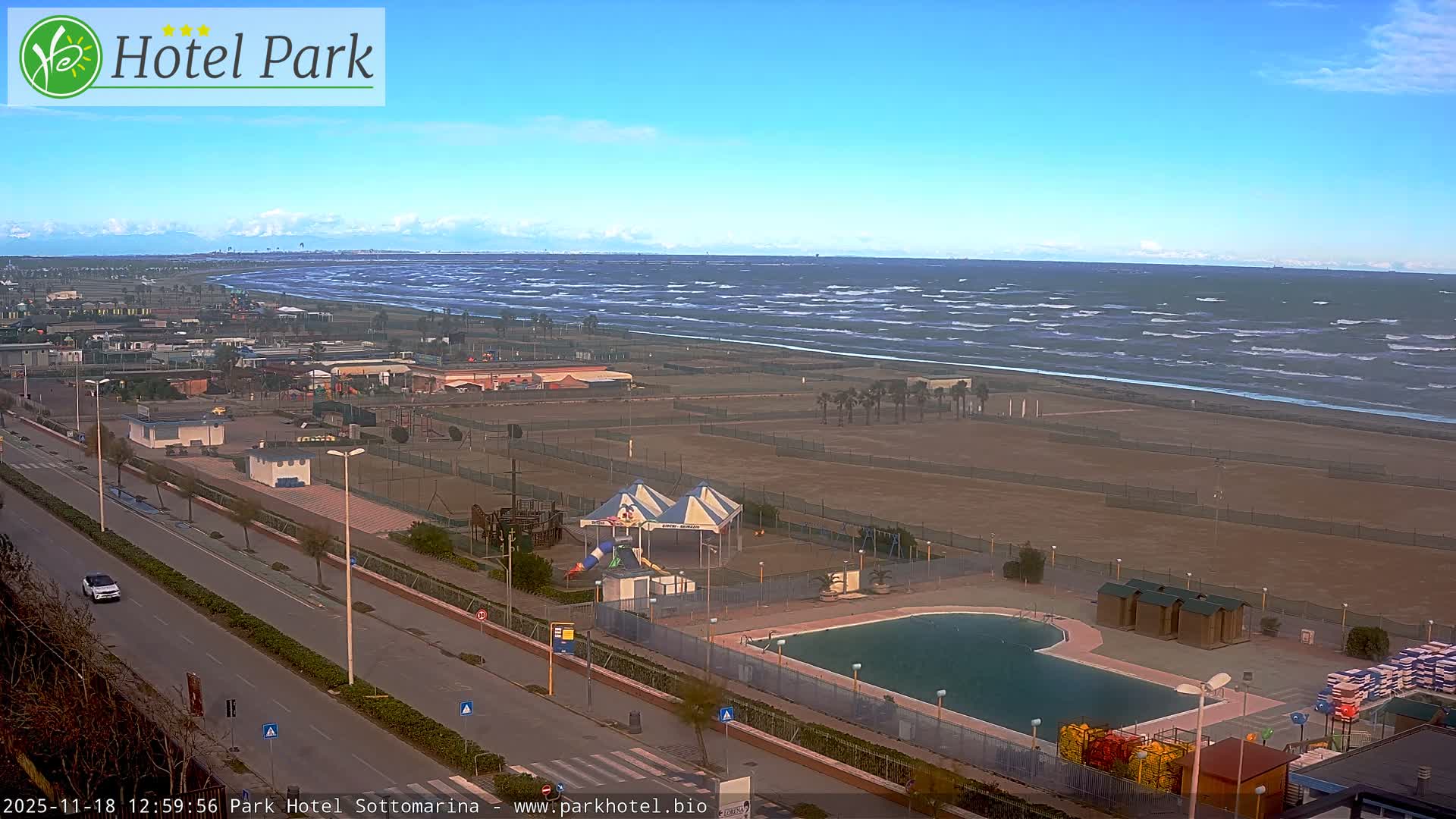 The image captures an outdoor night scene of a well-lit road and adjacent buildings bordering a dark expanse, likely a beach or open land, under a clear dark sky.