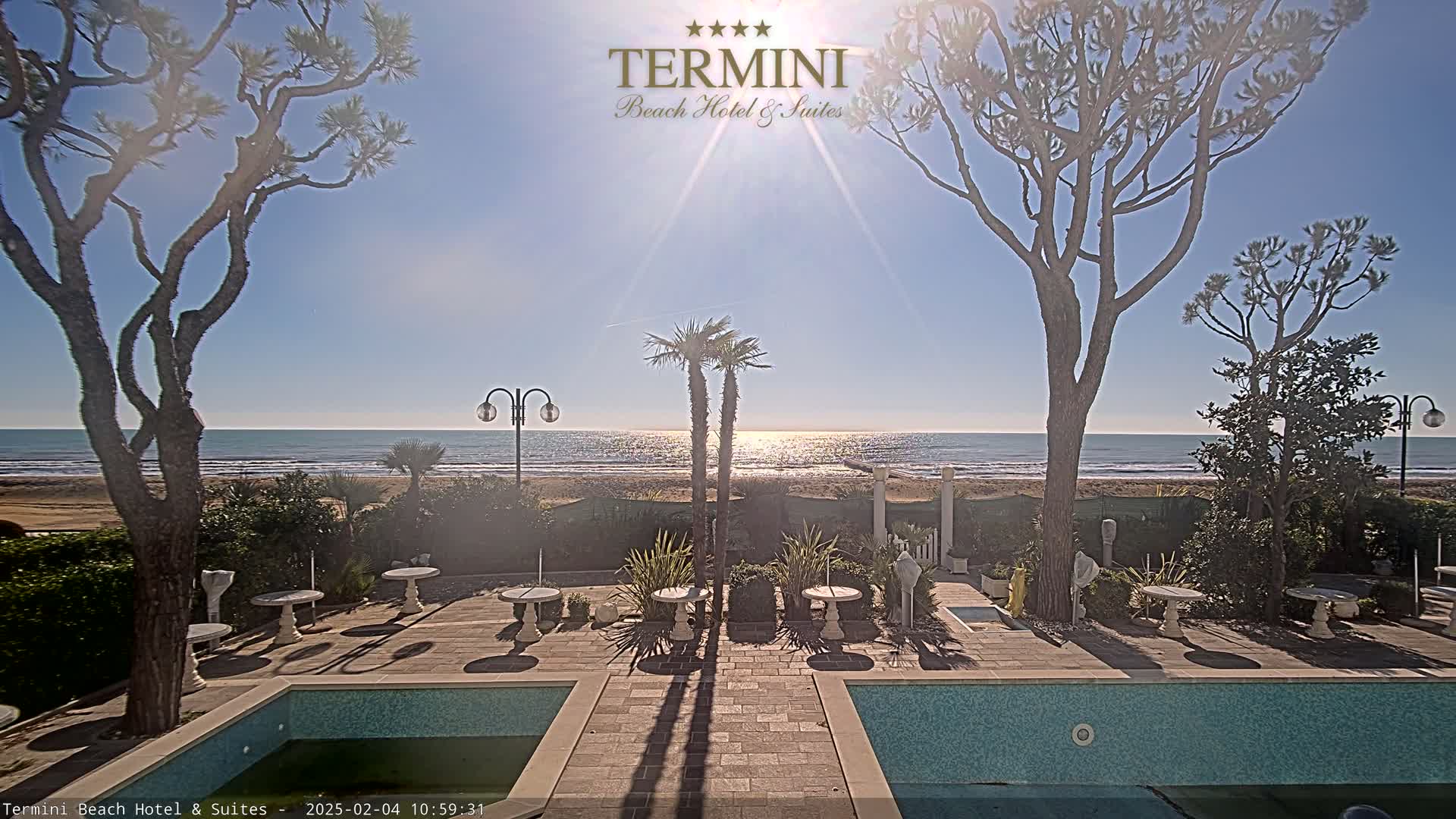 A sunny day at a beachfront hotel with a pool and patio furniture, overlooking a calm ocean.