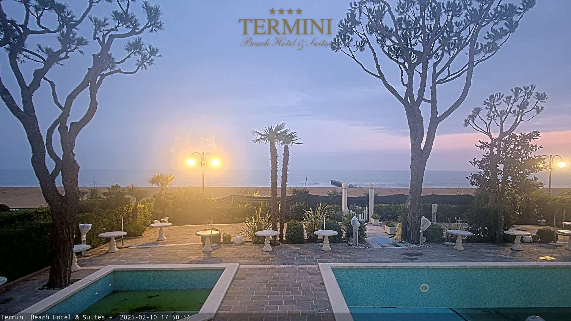 An outdoor patio area with two pools overlooks a calm ocean under a twilight sky.