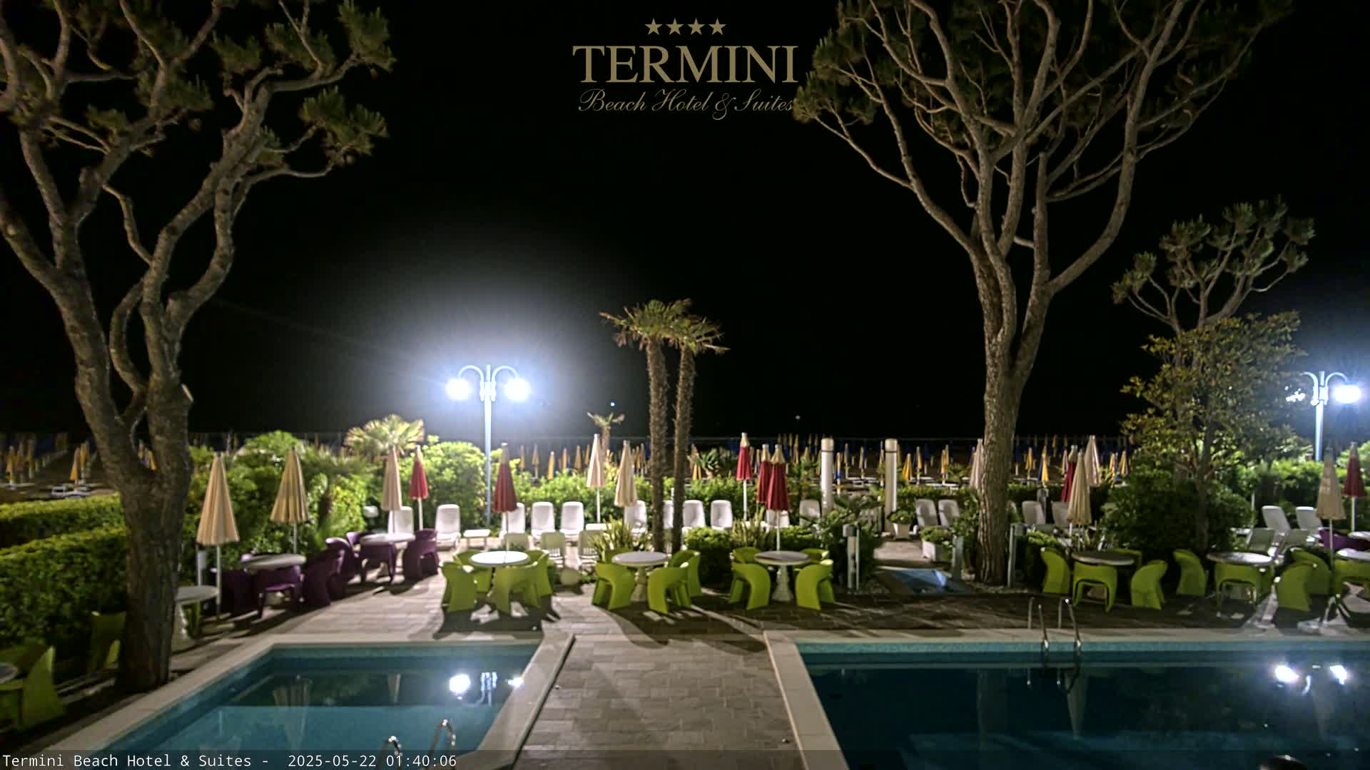 At night, a resort area with two pools and outdoor seating is illuminated under the dark sky.
