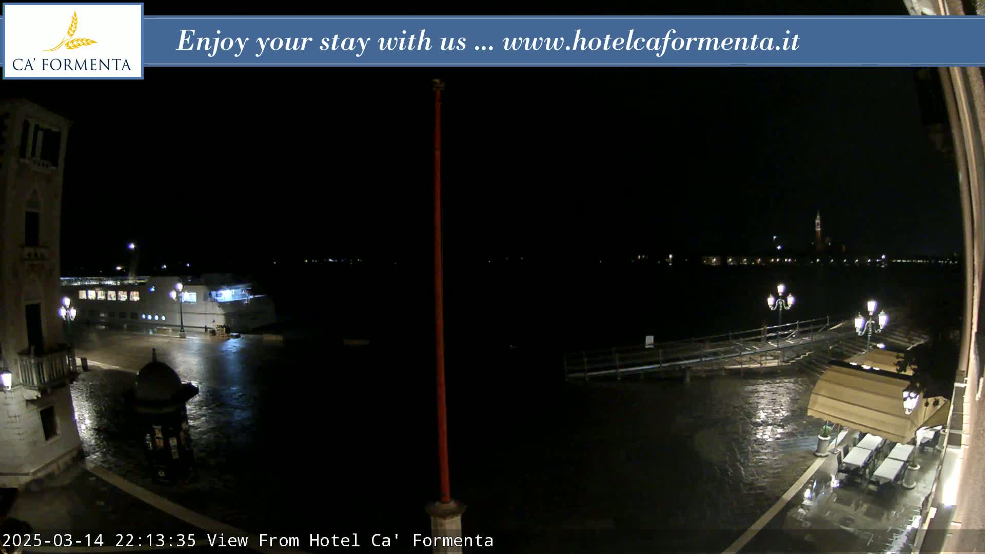 A nighttime view of a waterfront scene shows a large vessel moored near a building, with rain-slicked surfaces and lights illuminating the area.