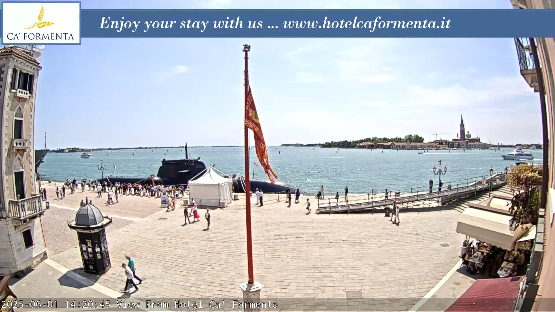 A submarine is docked near a waterfront plaza with people strolling around, under a sunny sky.