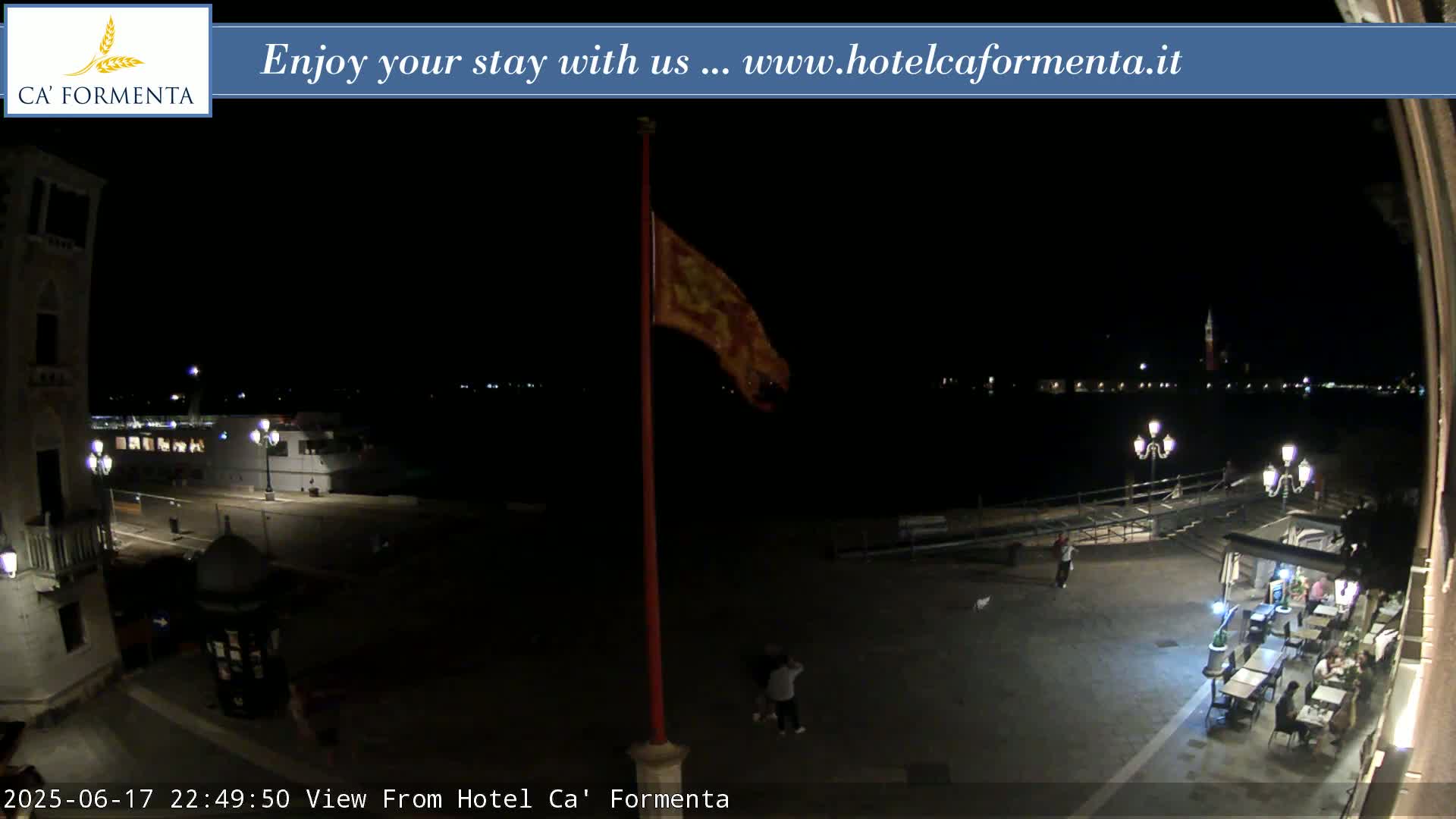 A nighttime view of a plaza overlooking a dark body of water, illuminated by streetlights and with a flag waving in the breeze.
