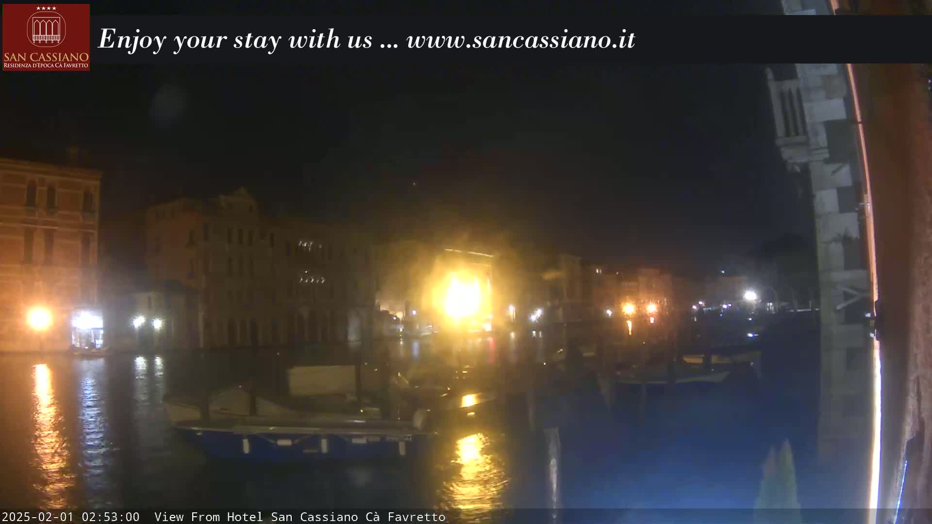 A nighttime view of a canal in Venice, showing buildings illuminated by lights reflecting on the water.