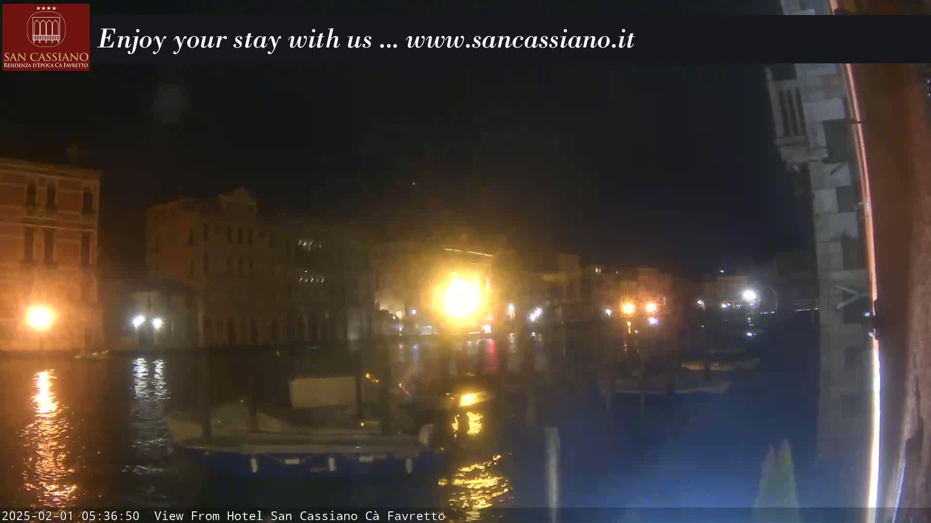 A nighttime view of a canal in Venice, showing illuminated buildings and boats on the water.