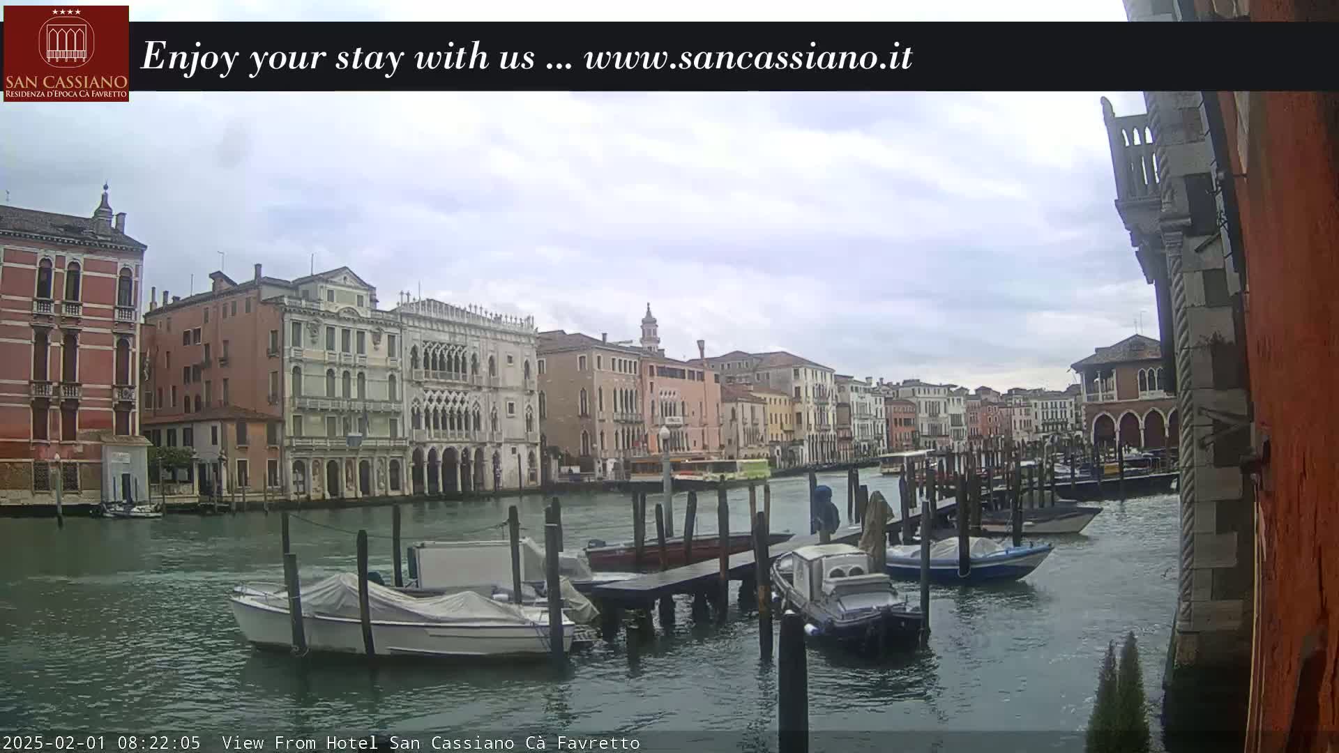 Several boats are moored along a canal in Venice, Italy, under a cloudy sky.