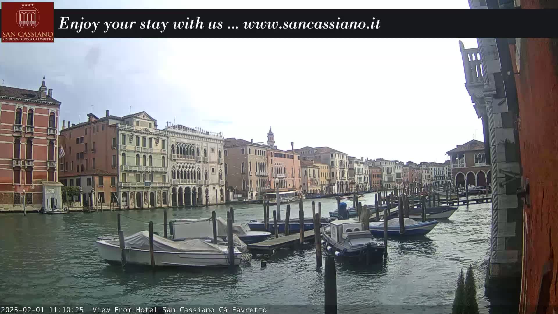Several boats are moored along a canal in Venice, Italy, under a cloudy sky.