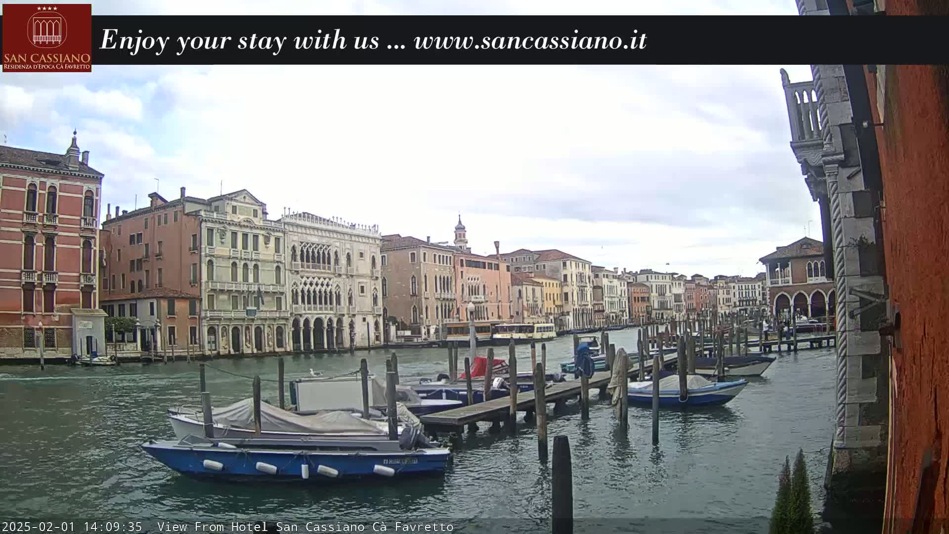 Several boats are moored at a dock along a canal in Venice, Italy, under a cloudy sky.