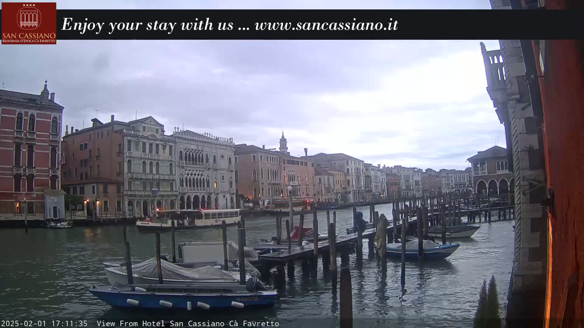 Several boats are moored at a dock along a canal in Venice, Italy, under an overcast sky.