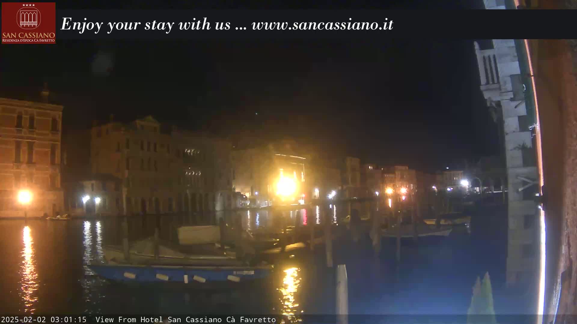 A nighttime view of a canal in Venice, with buildings illuminated along the waterfront.