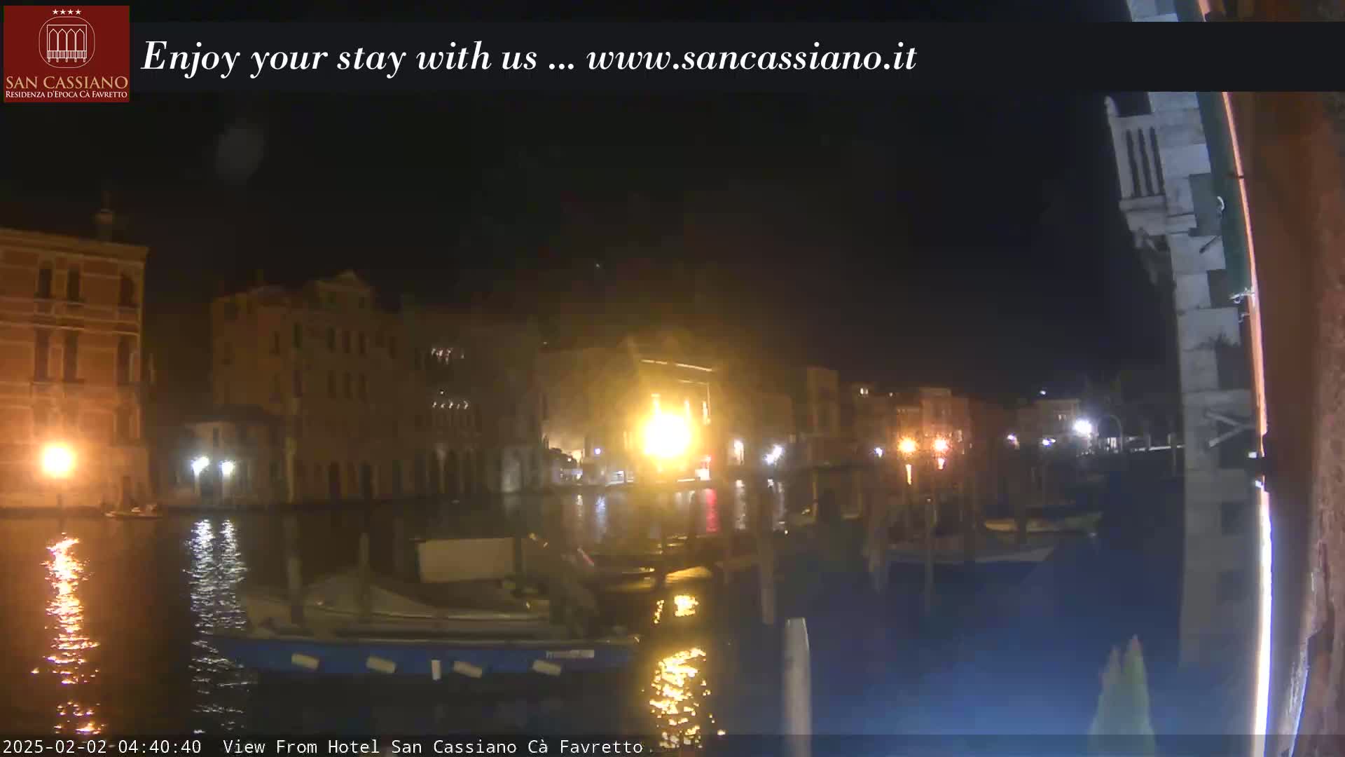 A nighttime view of a canal in Venice, with buildings lit up along its banks and boats moored on the water.