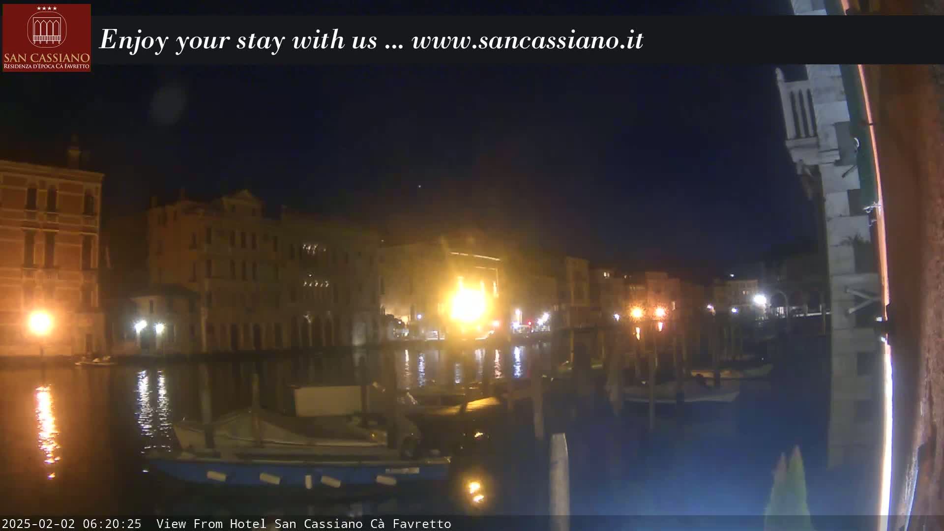 A nighttime view of a canal in Venice, Italy, shows several buildings illuminated along the waterway with boats moored near a stone structure.