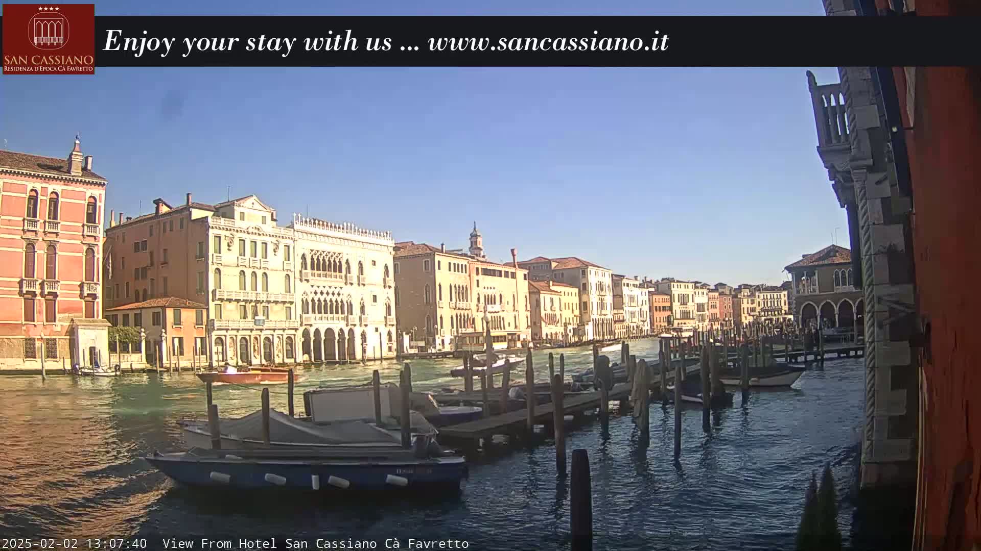 A sunny day in Venice shows a canal lined with colorful buildings and several boats moored at a dock.