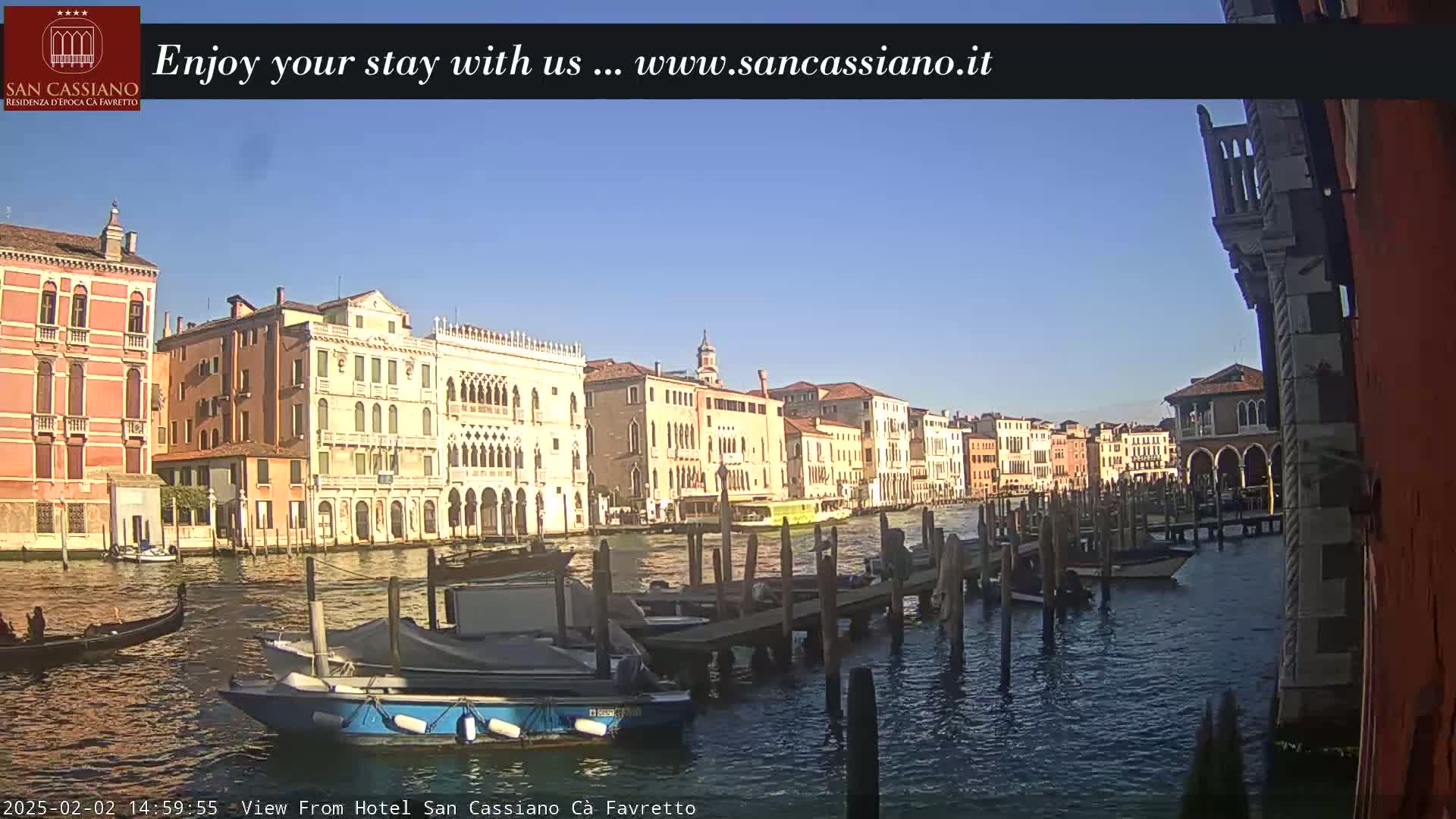 A sunny day in Venice shows colorful buildings lining a canal, with boats moored at a dock.