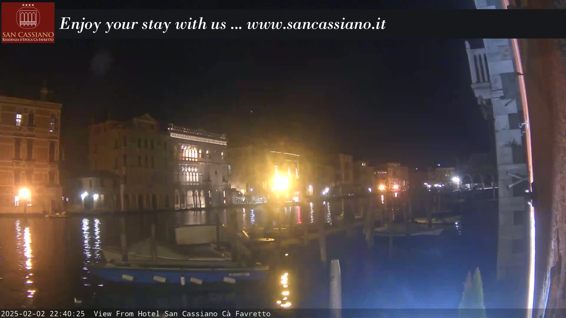 A nighttime view across a canal shows several illuminated buildings along the waterfront.