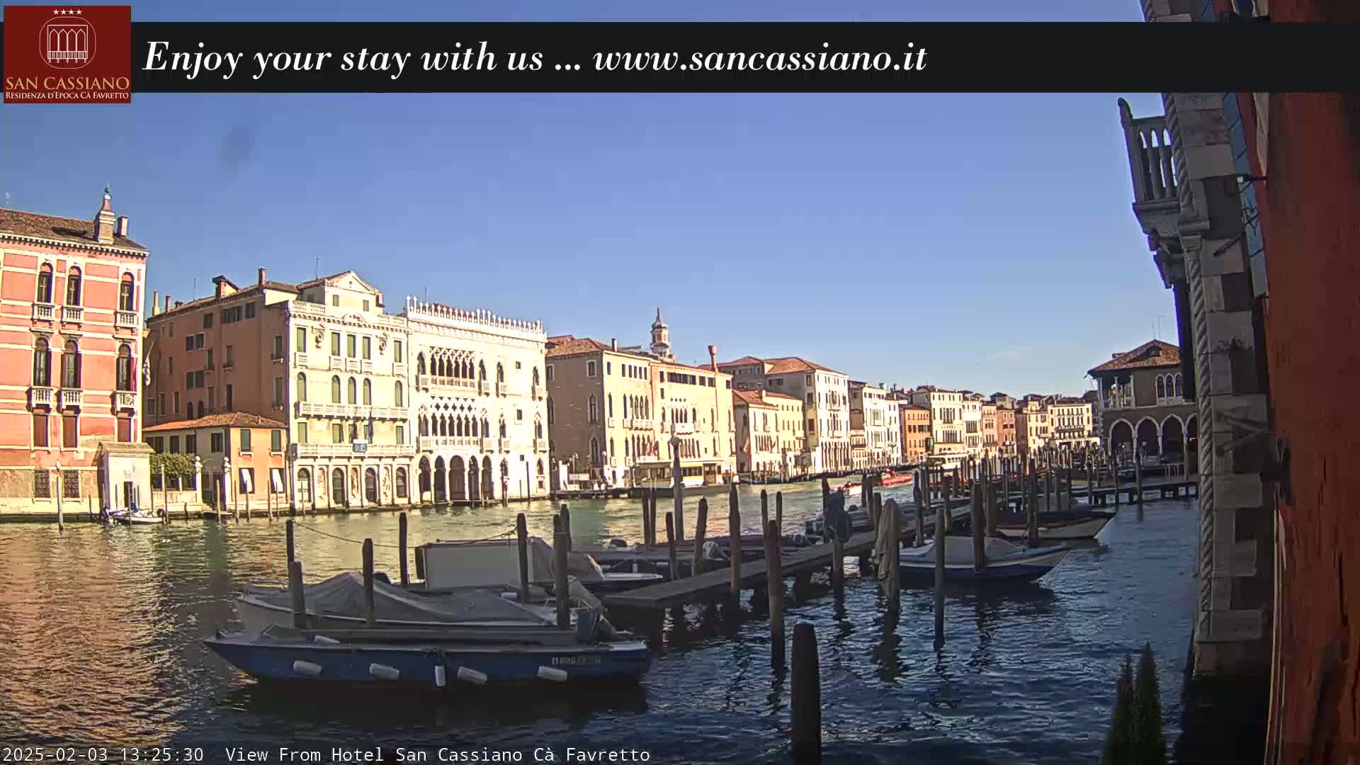 A sunny day in Venice shows a canal lined with historic buildings and several moored boats.