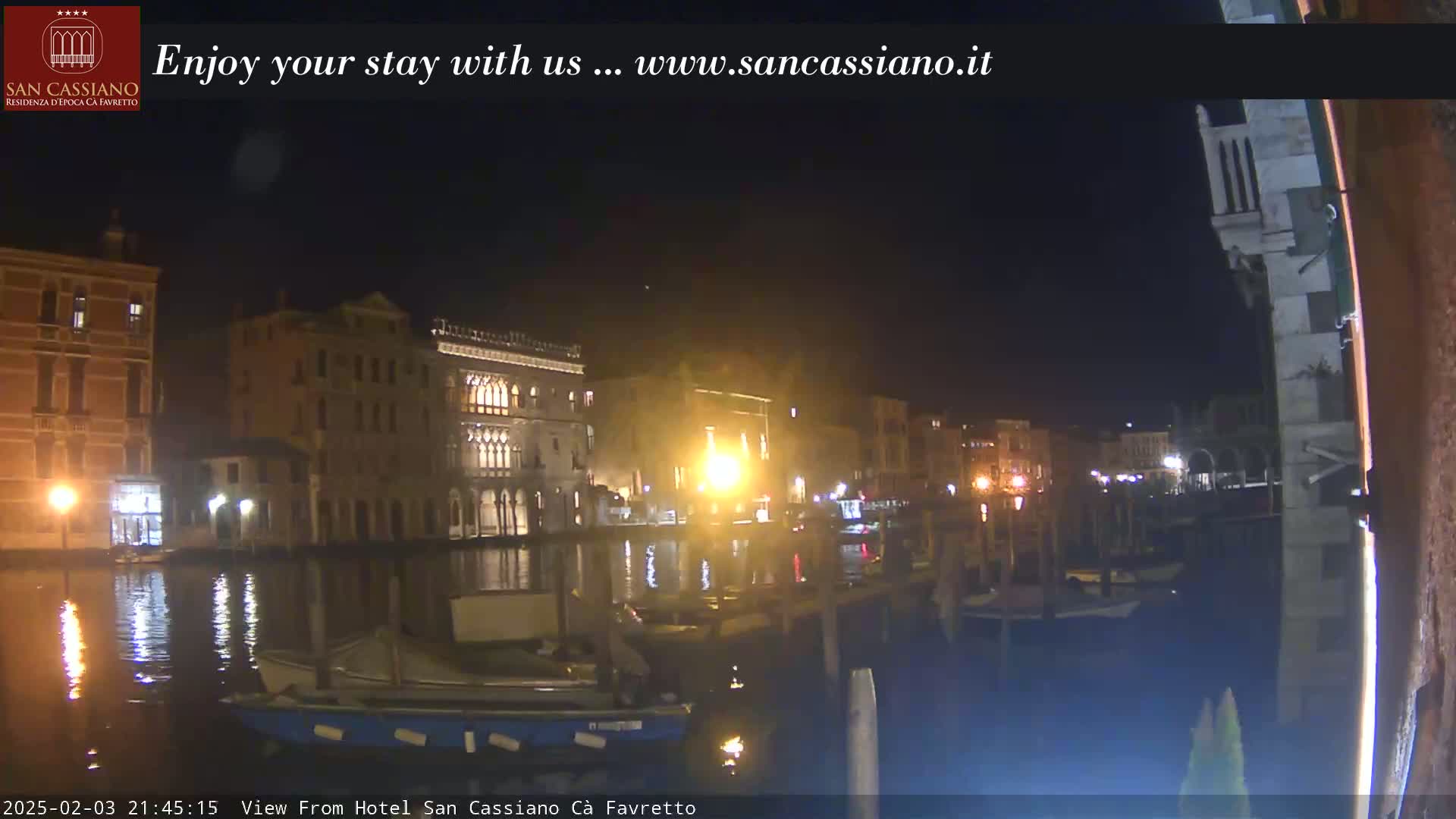 Nighttime view of illuminated buildings along a canal, with boats moored at a dock.