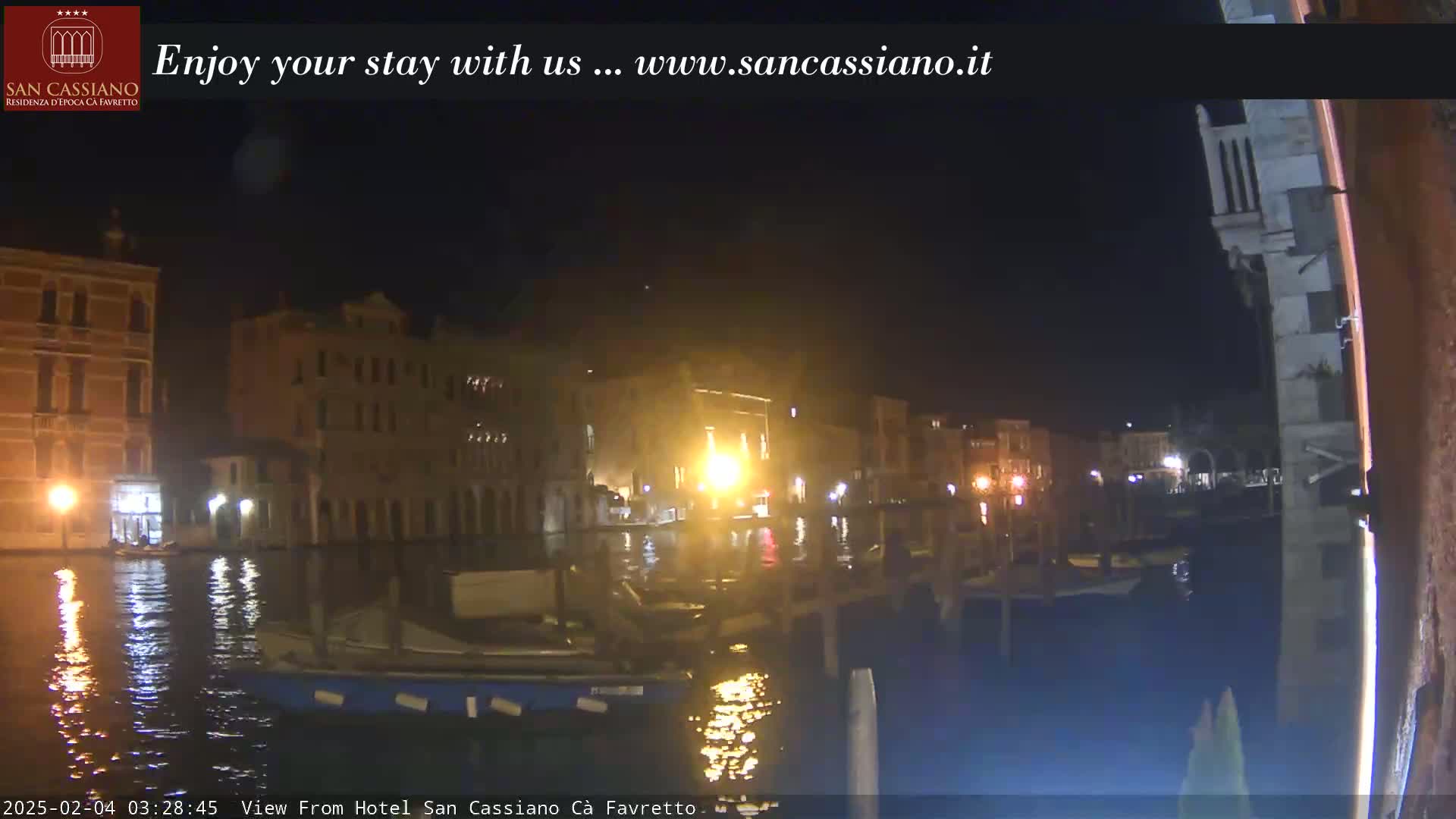 A nighttime view of a canal in Venice, showing illuminated buildings and boats along the water.