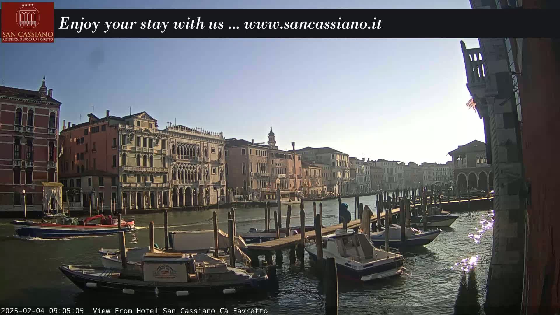 A sunny day in Venice shows a canal with moored boats and several buildings lining the waterway.