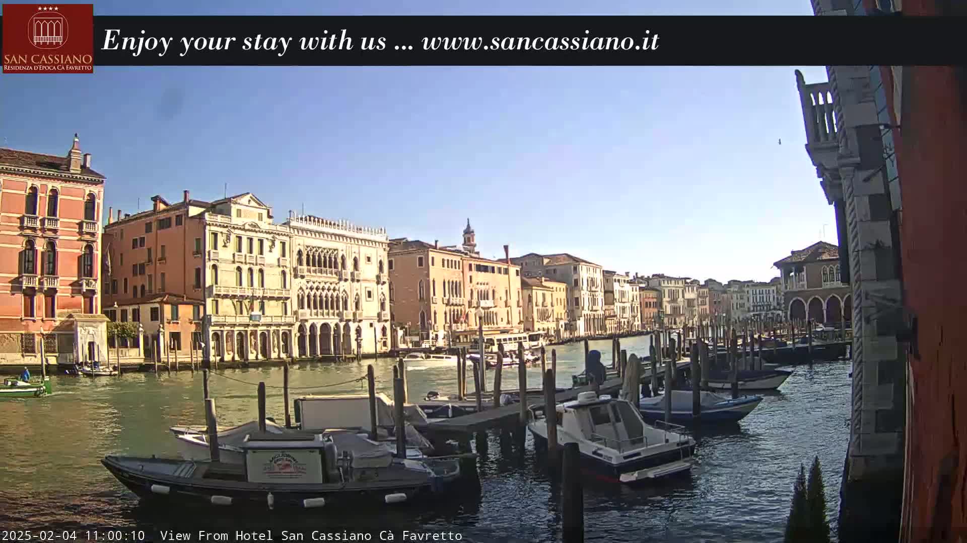 A sunny day in Venice shows a canal lined with historic buildings and numerous boats moored along the docks.