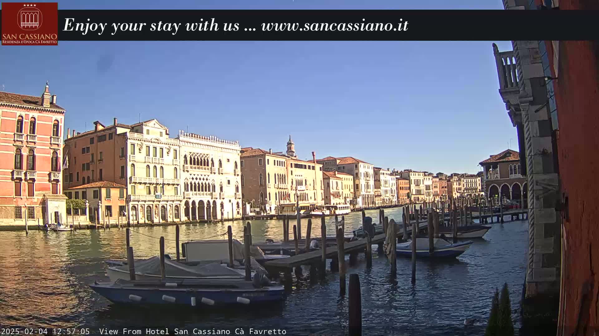 A sunny day reveals a Venetian canal lined with colorful buildings, boats moored at a dock, and calm water.