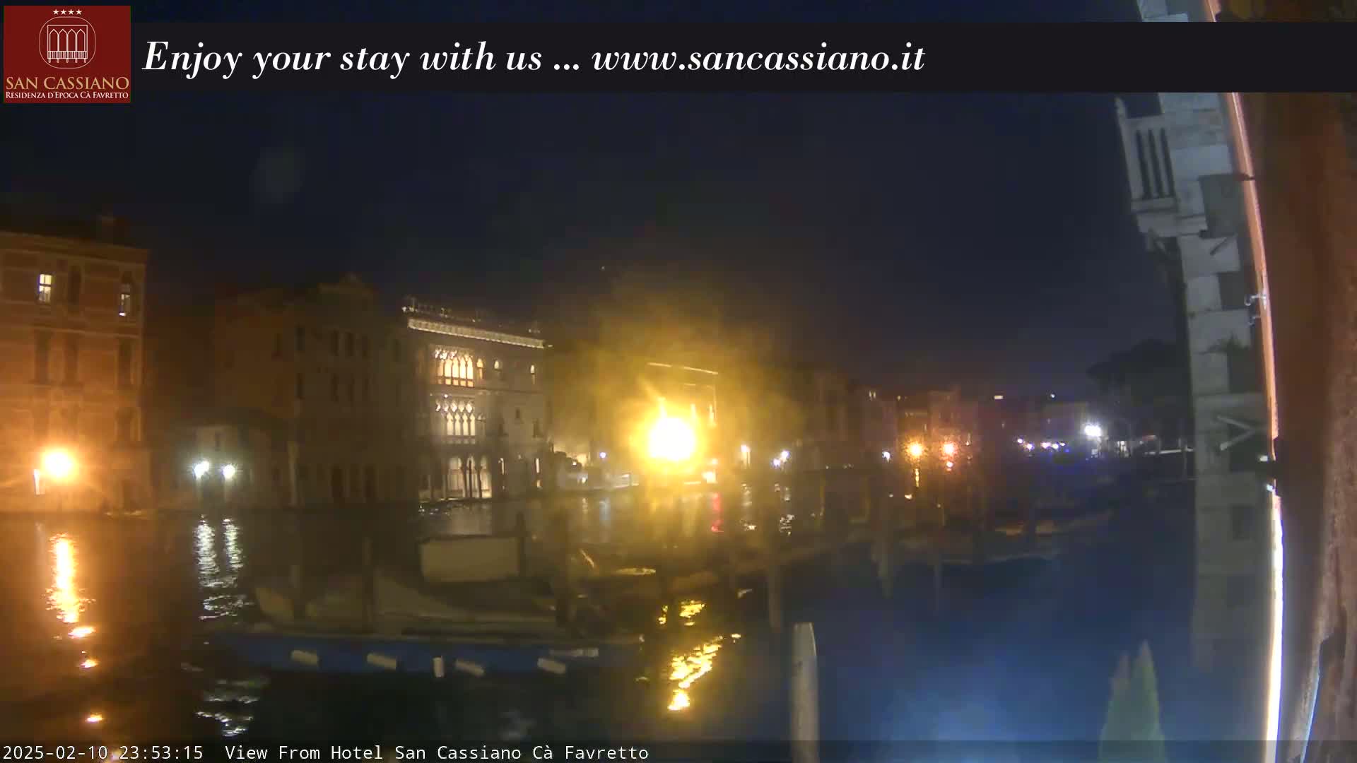 A nighttime view of a canal in Venice, showing illuminated buildings and boats on the water.