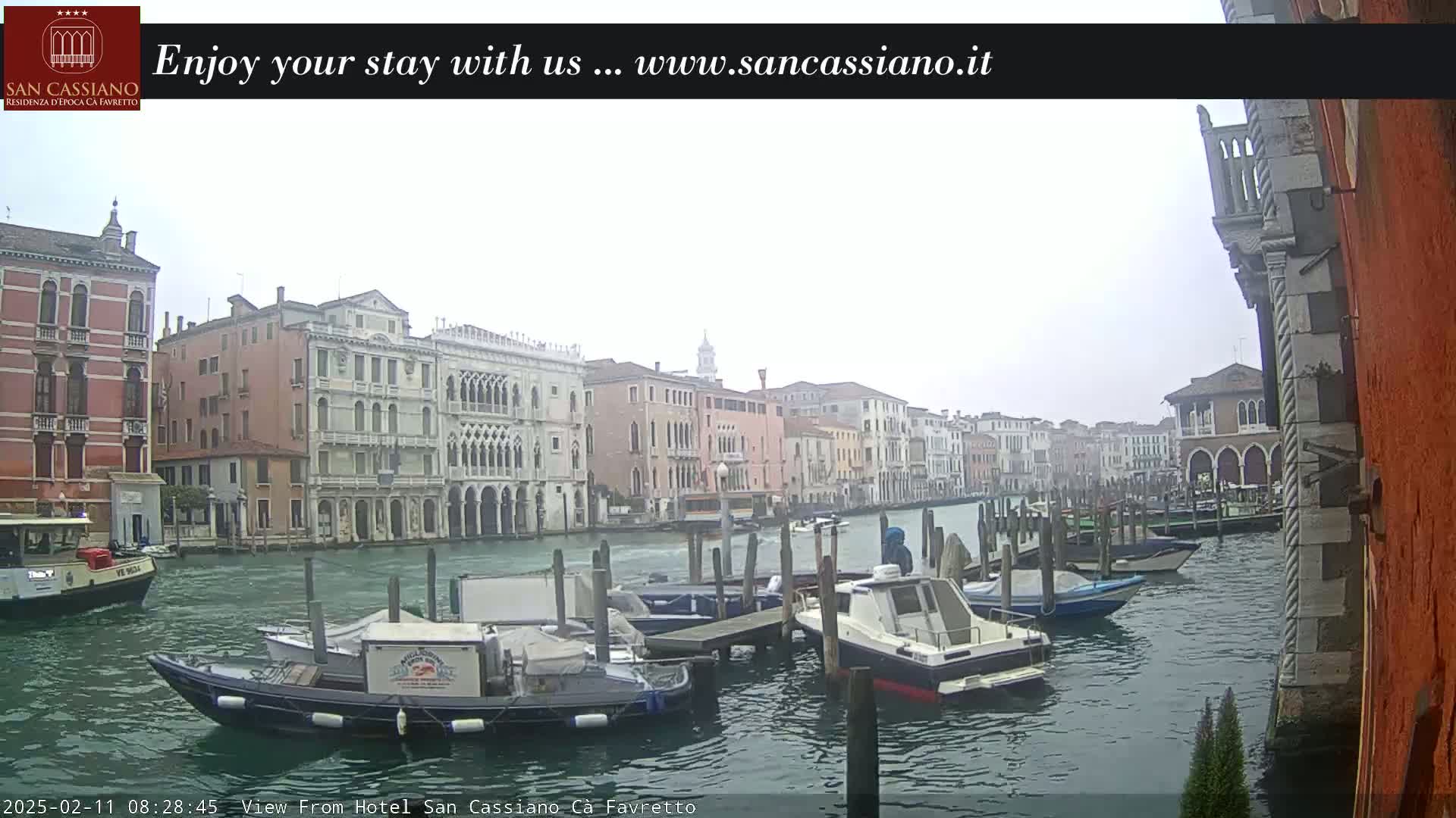 A view of a Venetian canal on an overcast day, showing several moored boats and buildings lining the waterway.