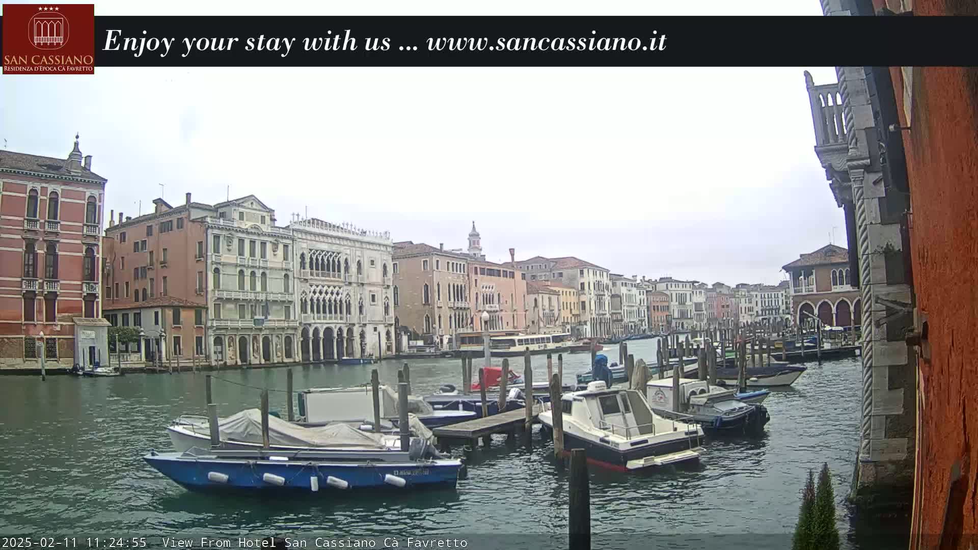 A cloudy day in Venice shows a canal lined with colorful buildings and several boats moored at a dock.