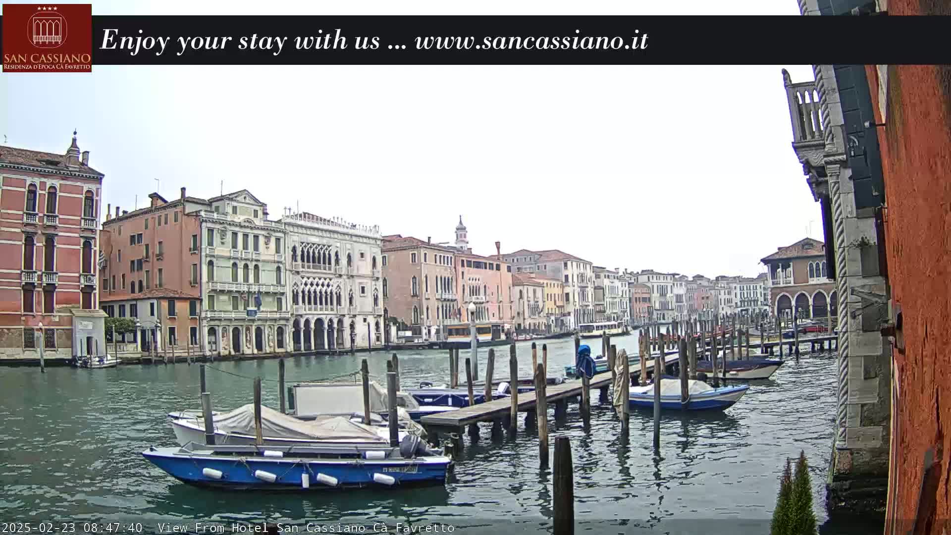 A cloudy day in Venice shows a canal with several moored boats and a line of buildings along the waterway.