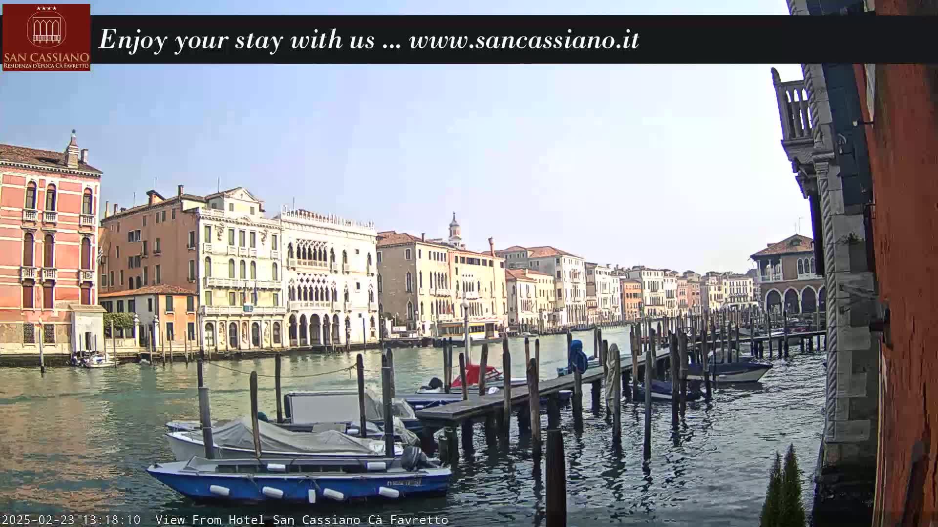 A sunny day in Venice shows several canal-side buildings and moored boats along a waterway.