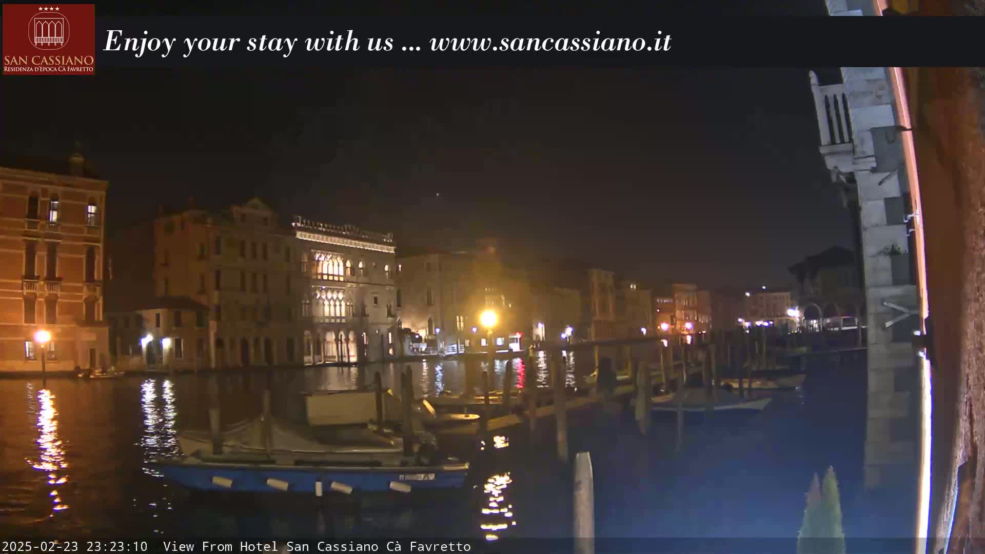 A nighttime view of a canal in Venice, with illuminated buildings lining the waterway and boats moored at the edge.