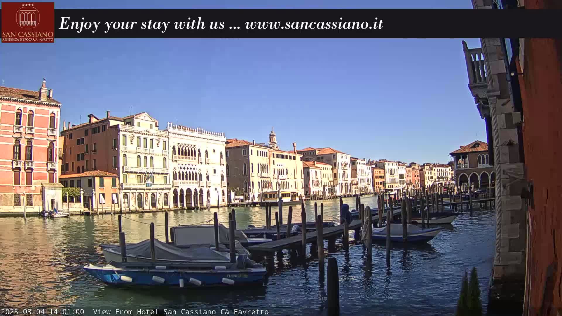 A sunny day in Venice shows a canal lined with colorful buildings and several moored boats.