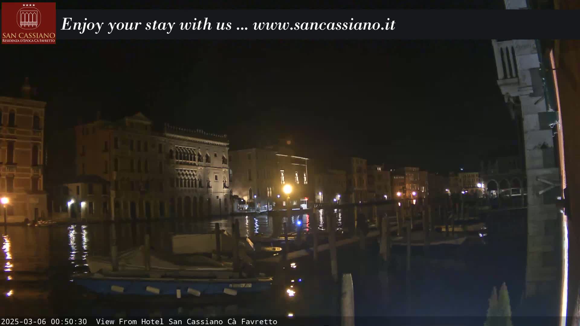 A nighttime view of a calm canal in Venice, showing illuminated buildings along the waterfront.
