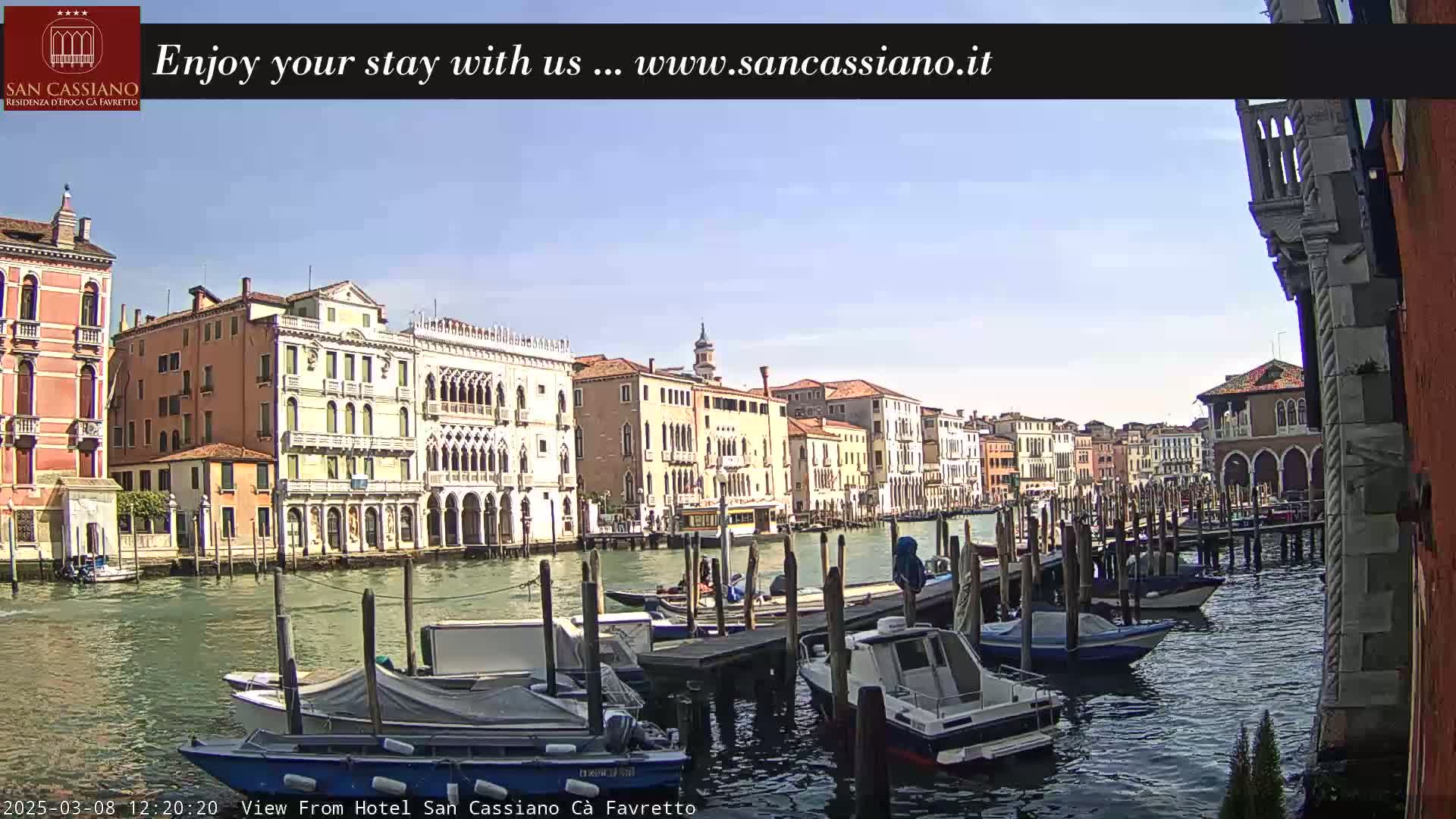 A sunny day in Venice shows a canal lined with historic buildings and numerous moored boats.