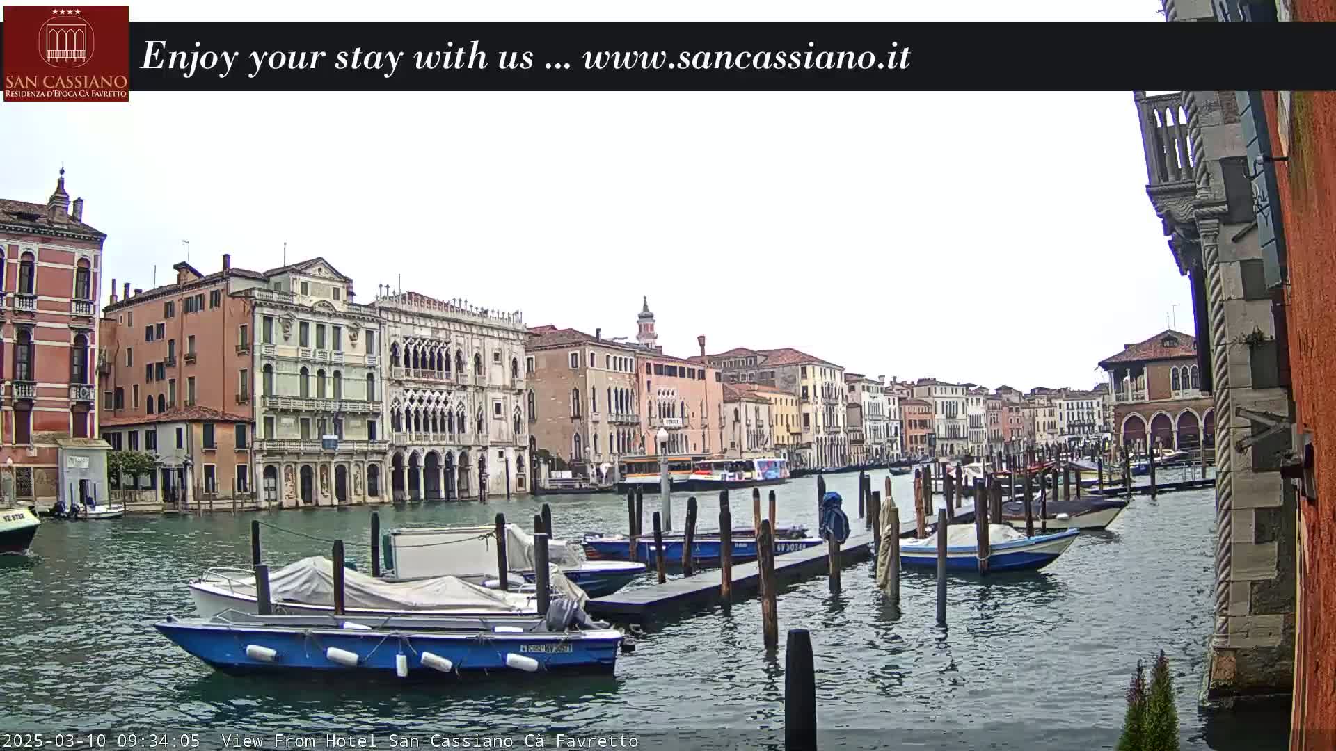 A canal in Venice, Italy, with overcast skies, is lined with colorful buildings and numerous moored boats.