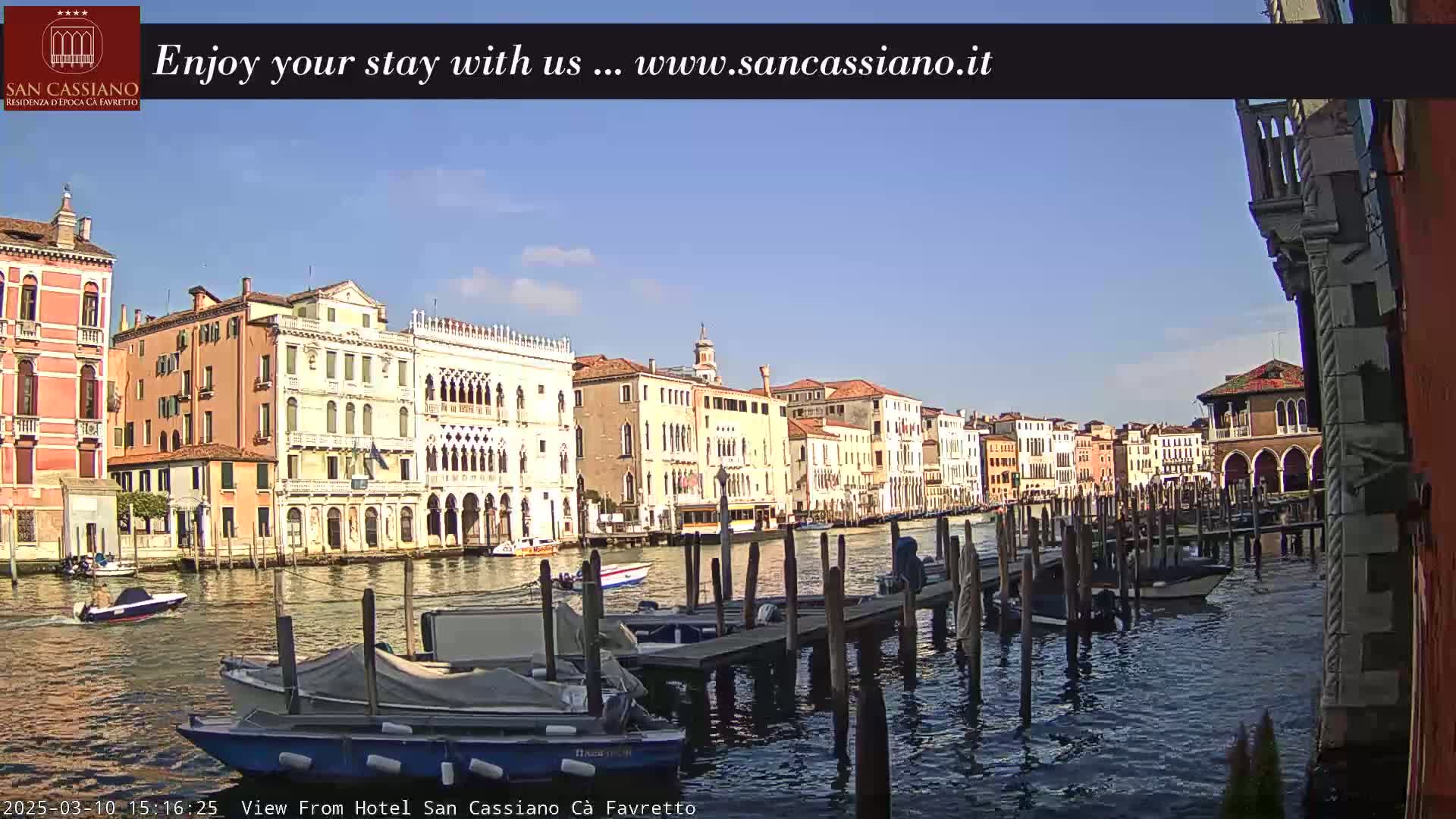 A sunny day in Venice shows several colorful buildings lining a canal with boats moored at wooden docks.