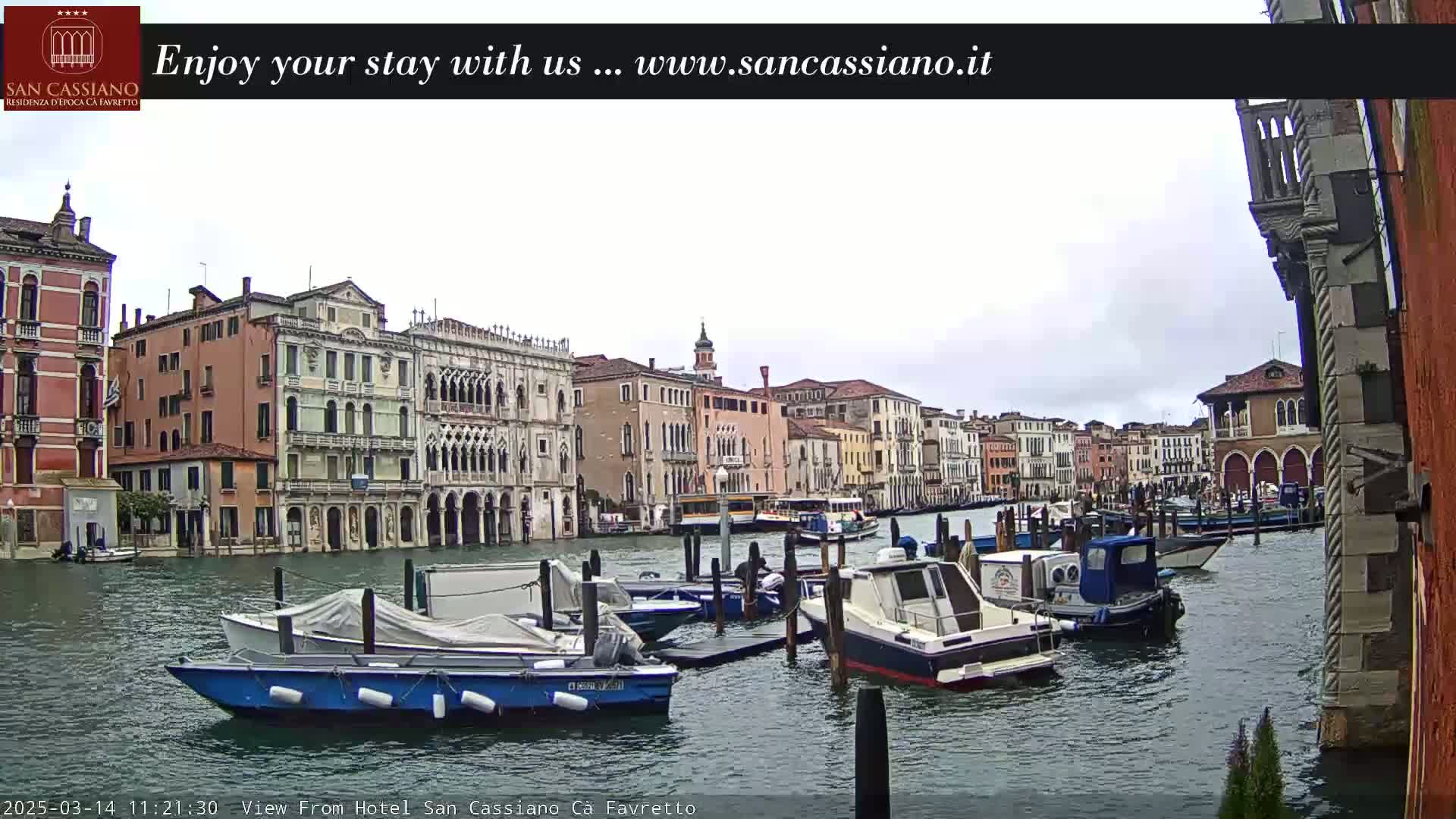 Several boats are moored along a canal in Venice, Italy, under an overcast sky.