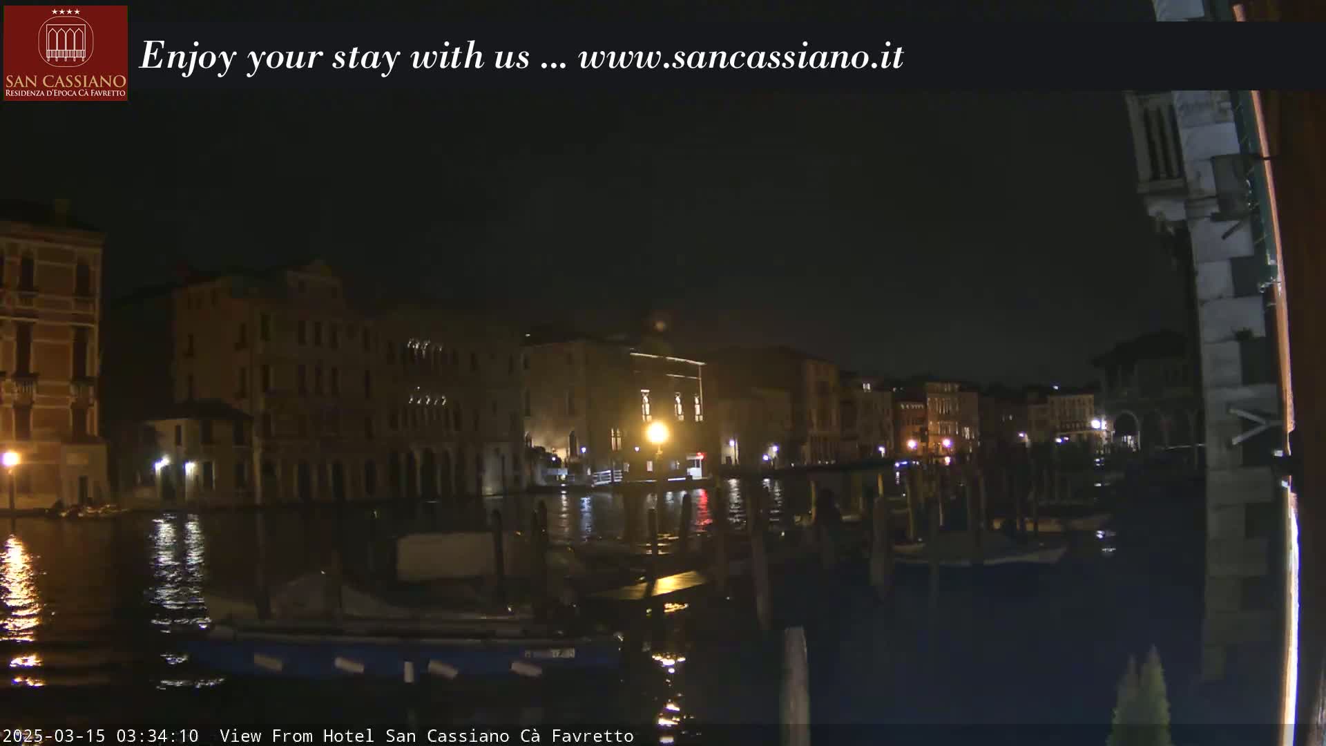 A nighttime view of a canal in Venice, with several buildings illuminated along the waterway.