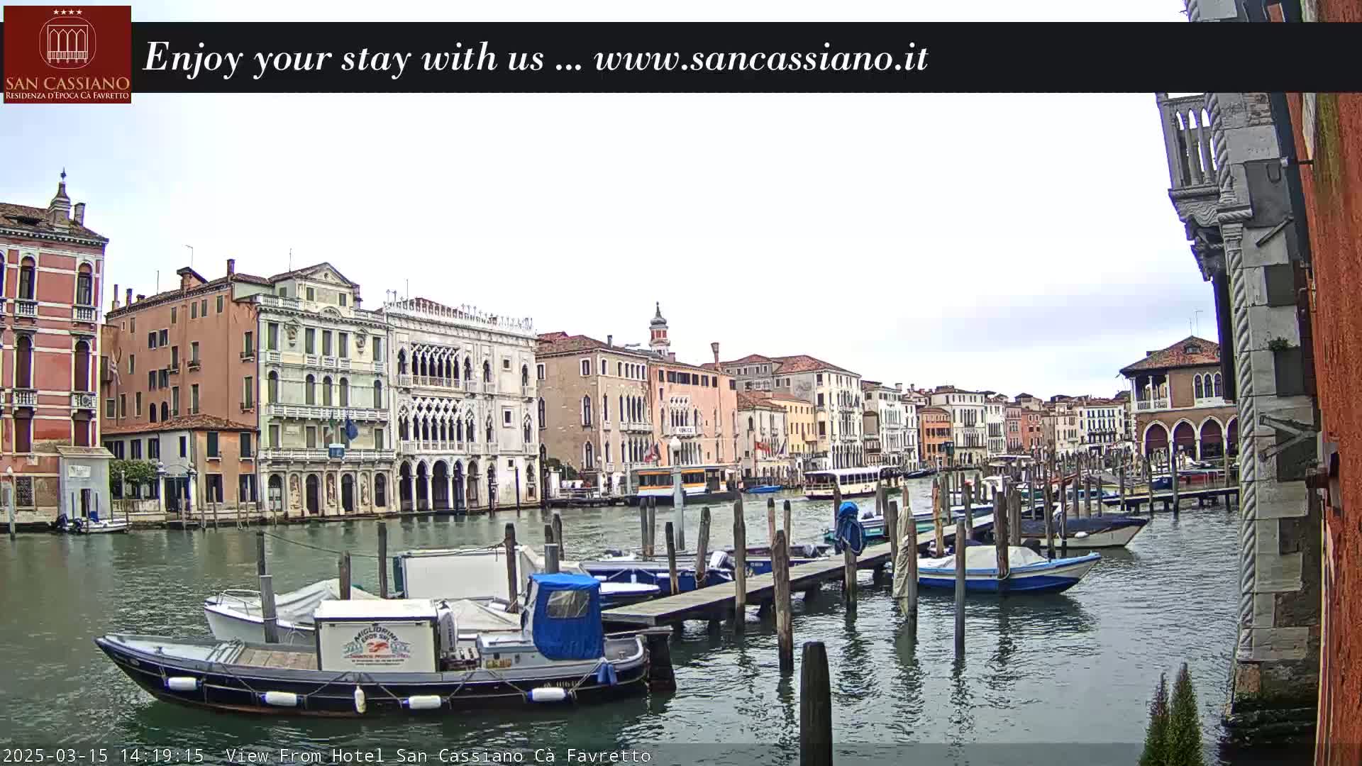 A cloudy day in Venice shows a canal with numerous boats moored at a dock in front of several historic buildings.