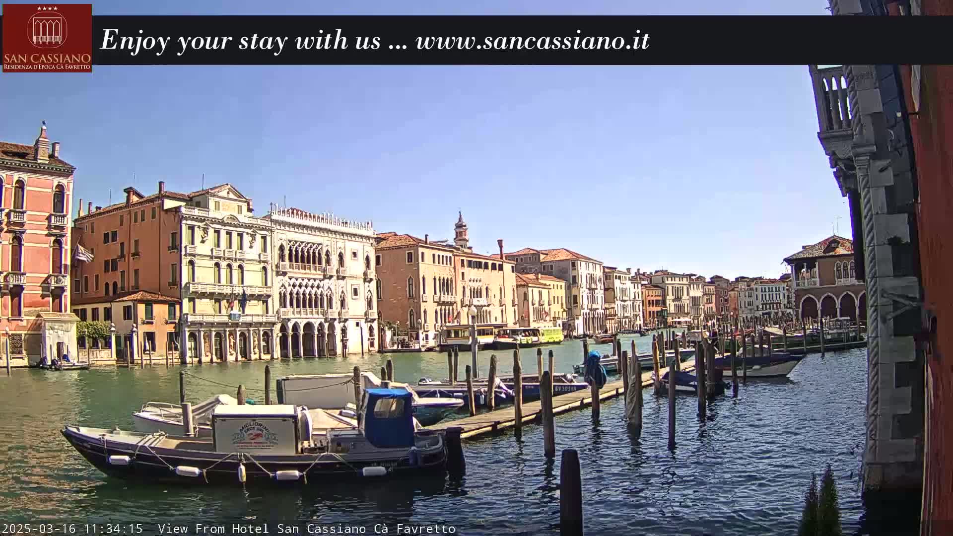 A sunny day in Venice shows a canal lined with colorful buildings and numerous boats moored at a dock.