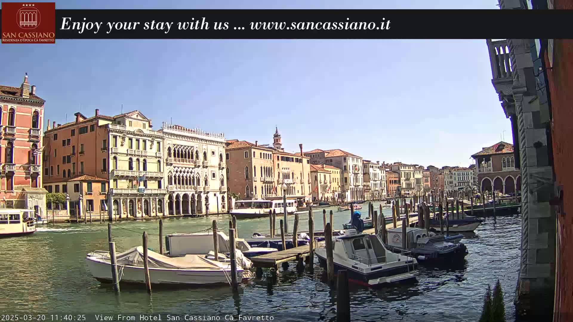 A sunny day in Venice shows a canal lined with historic buildings and moored boats.