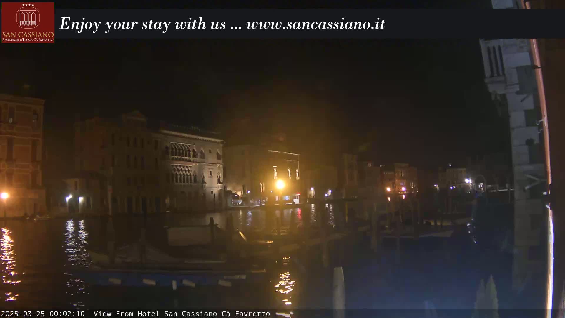 A nighttime view of a canal in Venice, showing illuminated buildings along the waterway.