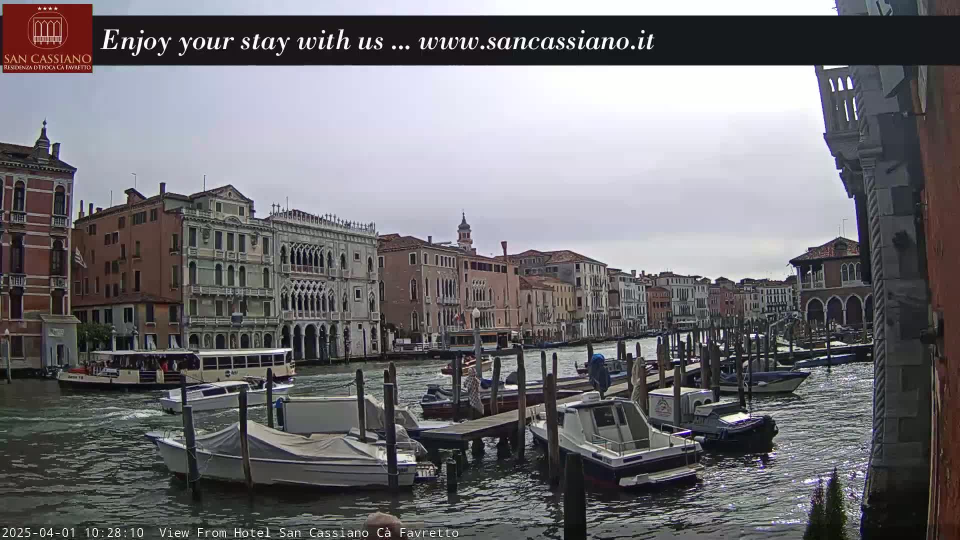 A canal in Venice, under an overcast sky, is lined with historic buildings and numerous moored boats.