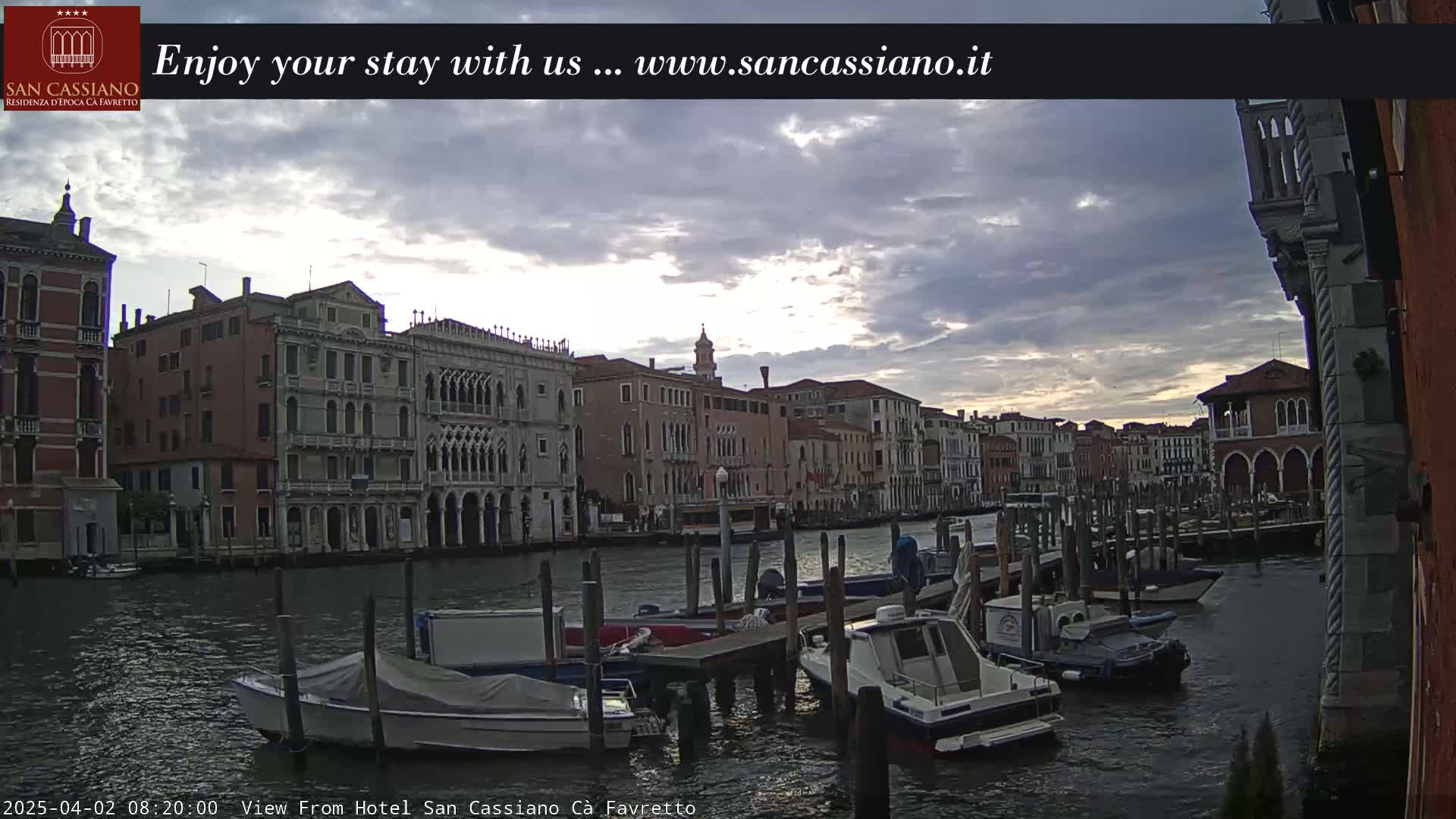 A cloudy sunset illuminates a Venetian canal lined with historic buildings and numerous moored boats.