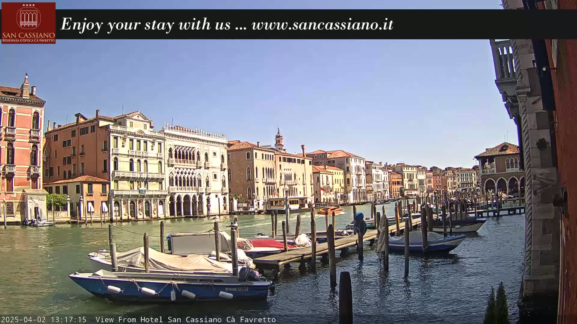 A sunny day in Venice shows a canal lined with historic buildings and several moored boats.