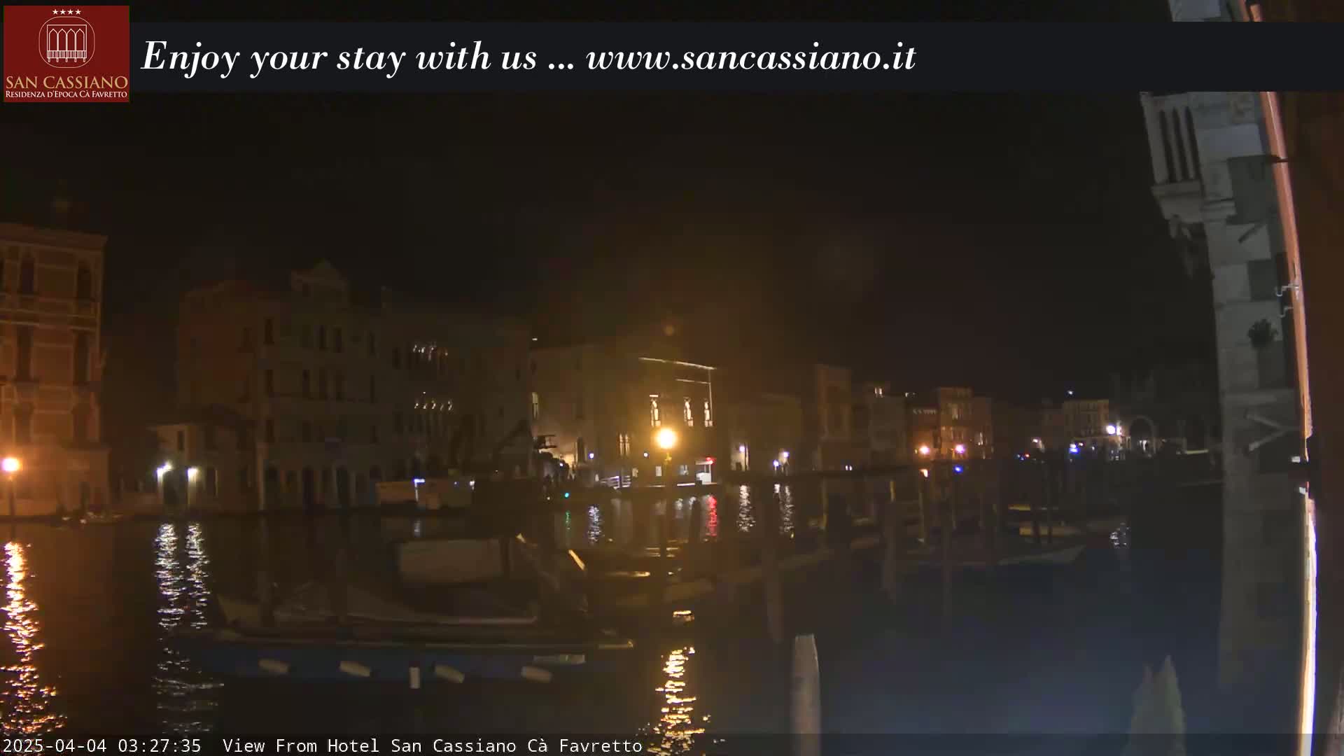 A nighttime view from a hotel shows a canal with boats and buildings along its banks.