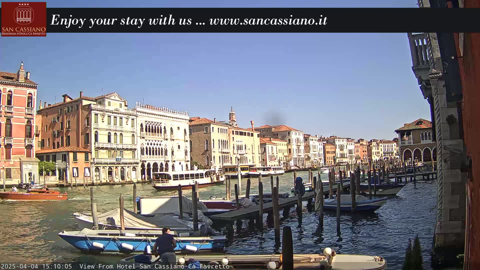 A sunny day in Venice shows a canal lined with moored boats and colorful buildings.