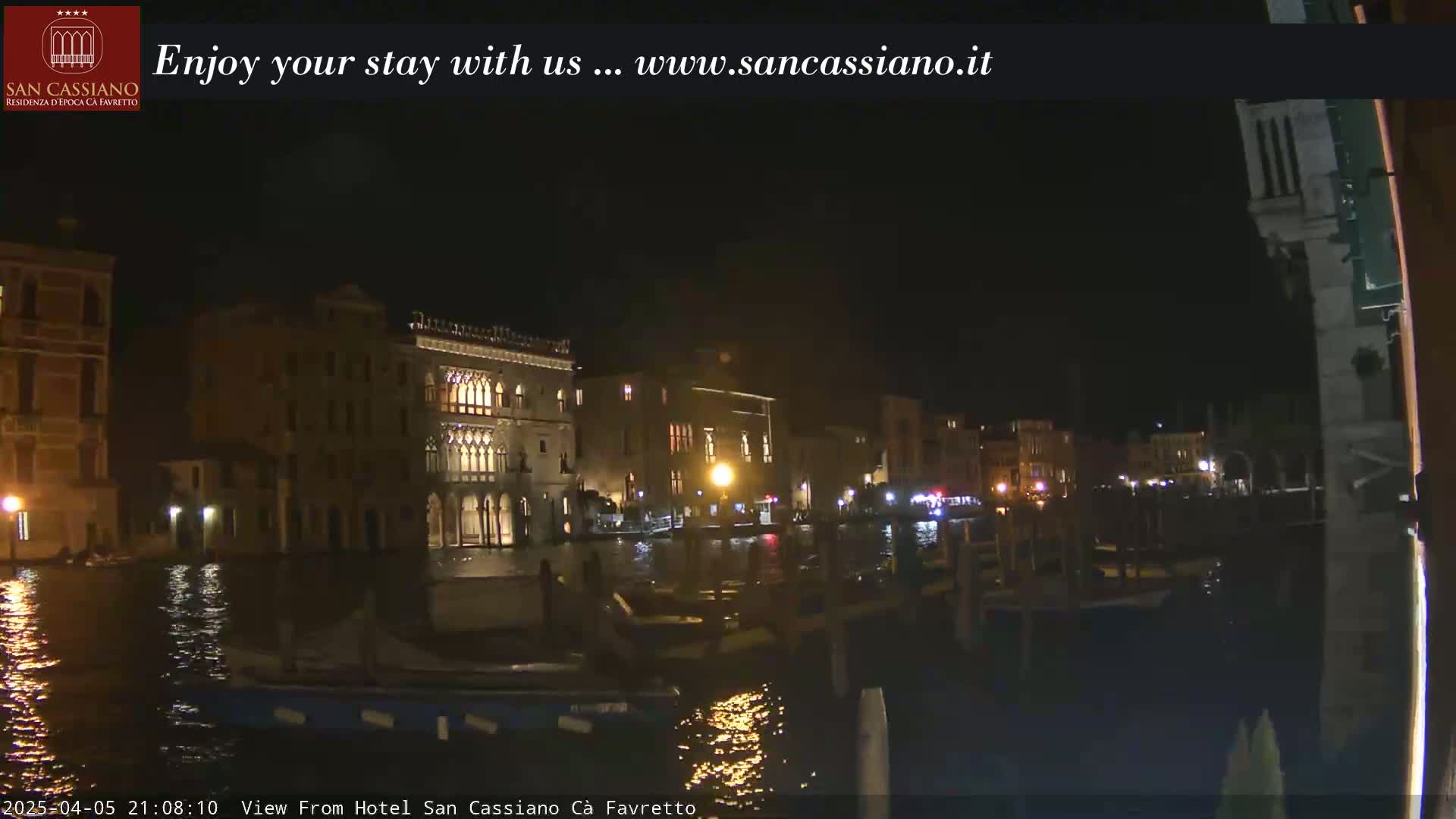 A nighttime view of buildings along a canal, with boats moored nearby, under a clear, dark sky.